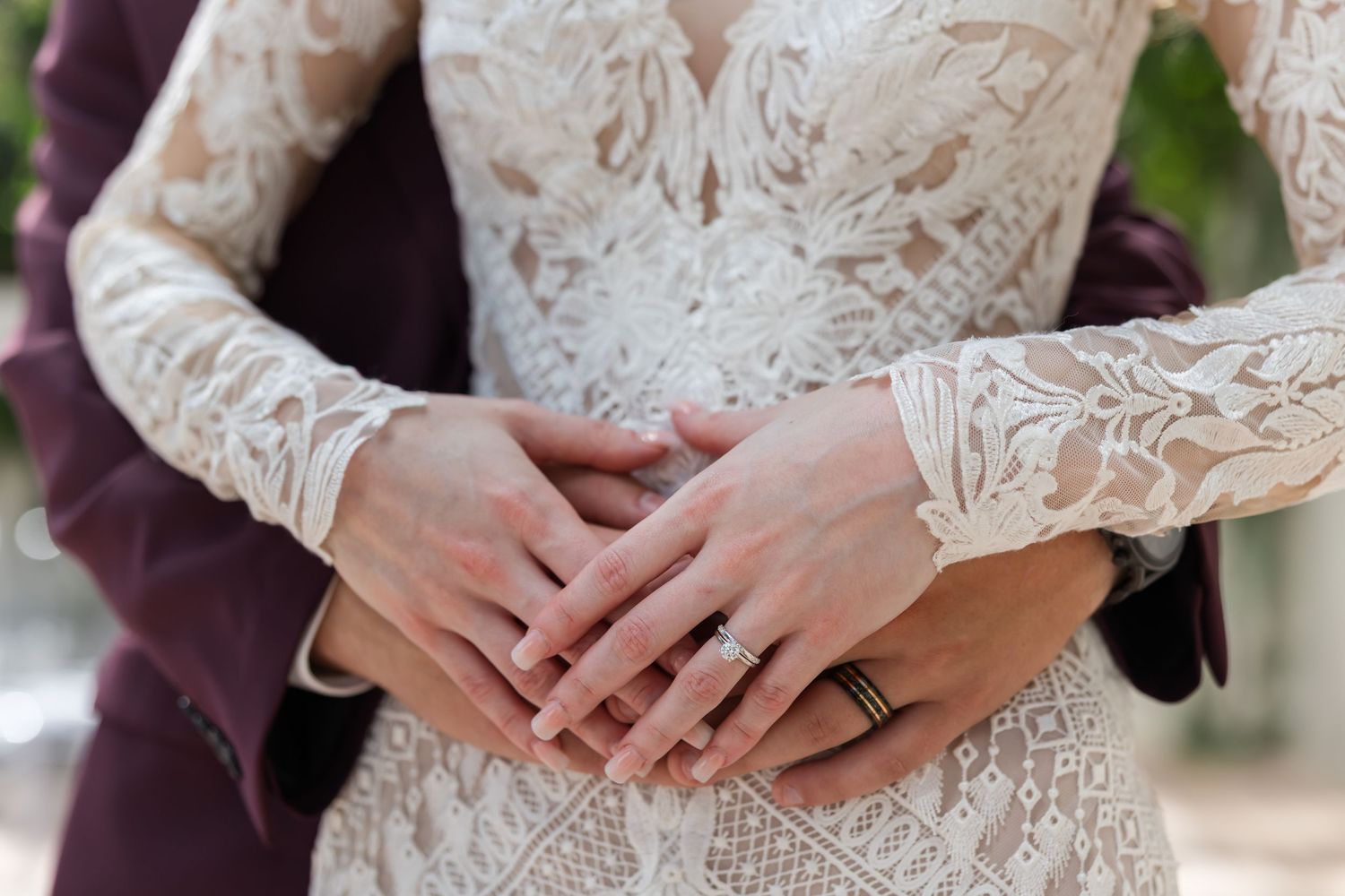 Close-up of bride and groom hands with wedding rings on elegant lace wedding dress.