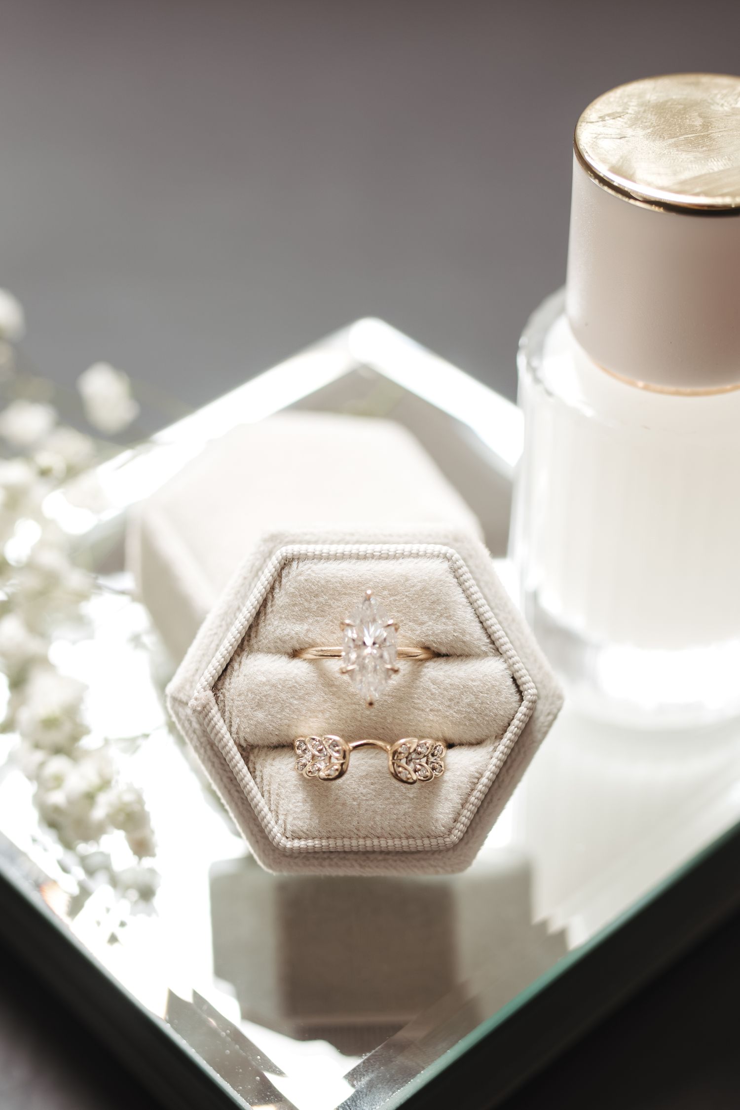 Delicate engagement ring and wedding bands displayed in hexagonal ring box with perfume bottle.