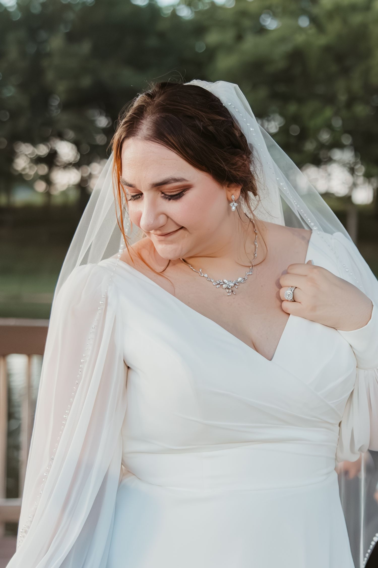 A bride in an elegant white v-neck wedding dress and veil smiles while wearing delicate jewelry.
