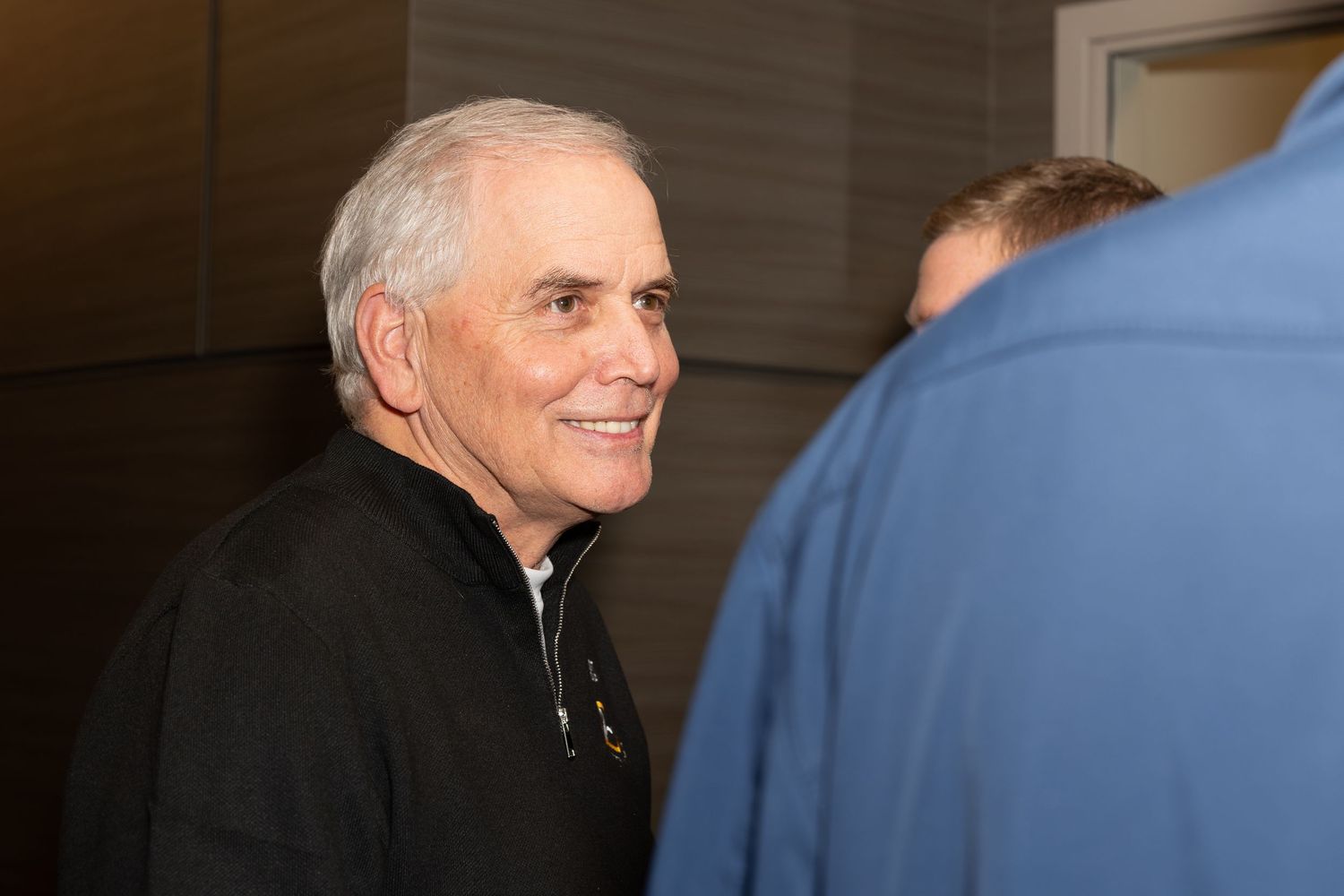 Person in black jacket engaged in friendly conversation at indoor event.