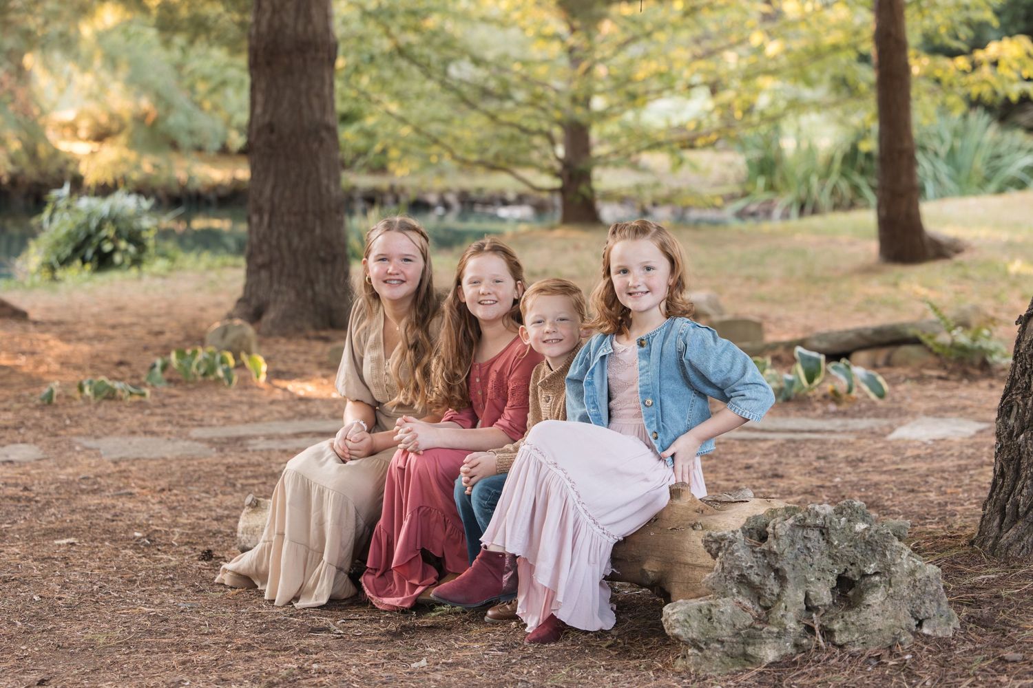 Four children sit together on a log in a forest during autumn.
