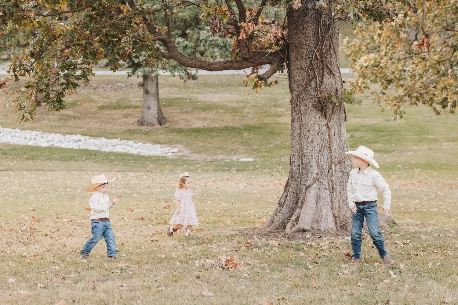 Children playing and running around a large tree in a park setting.
