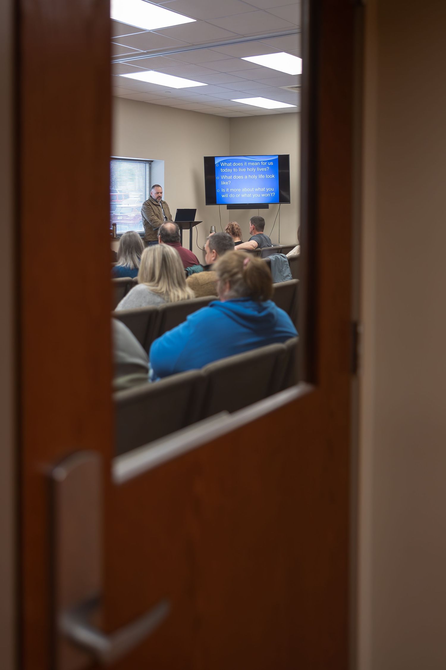 View through doorway of classroom with presentation screen and audience.