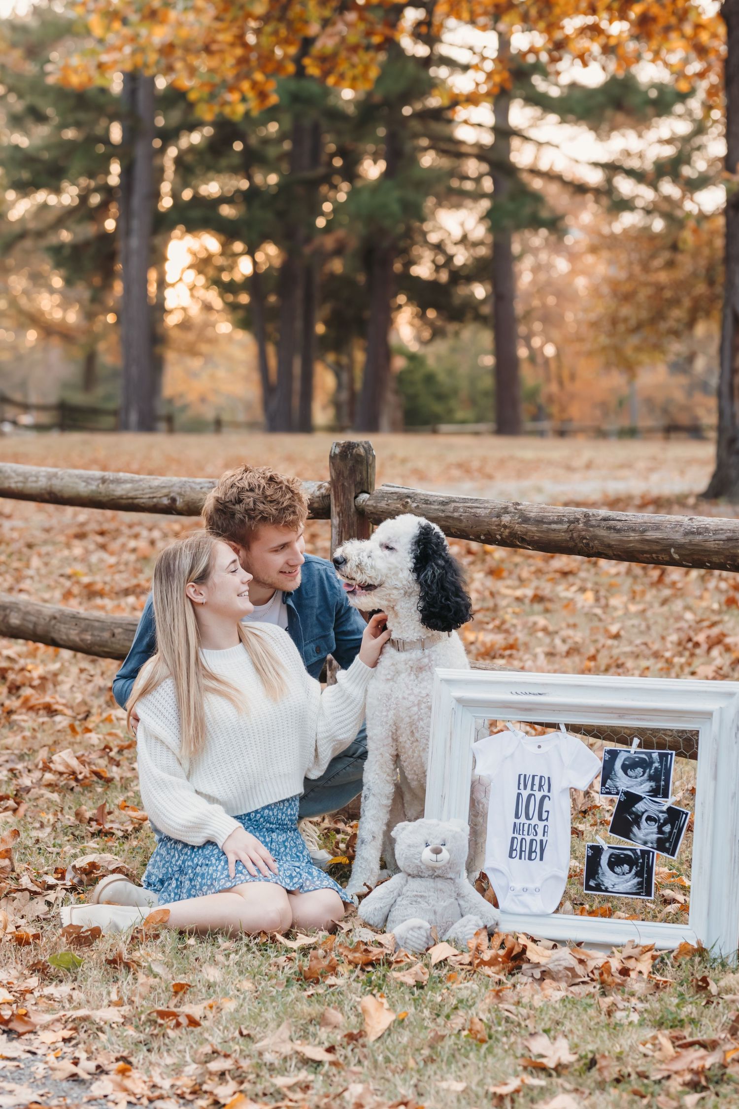 Couple with their dog sharing pregnancy announcement with ultrasound photos in fall setting.