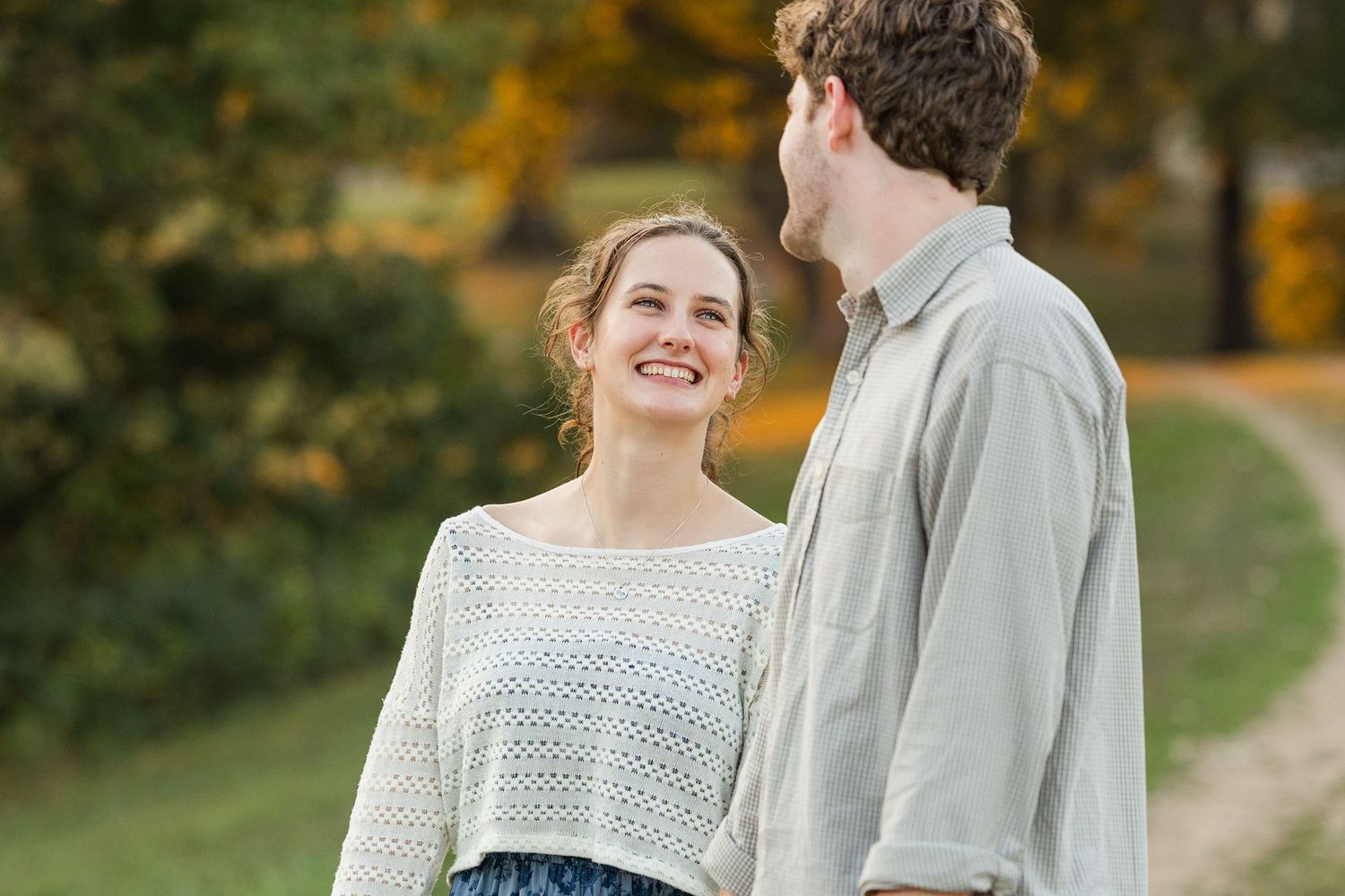 A couple shares a tender moment together on a path during autumn with fall foliage in the background.