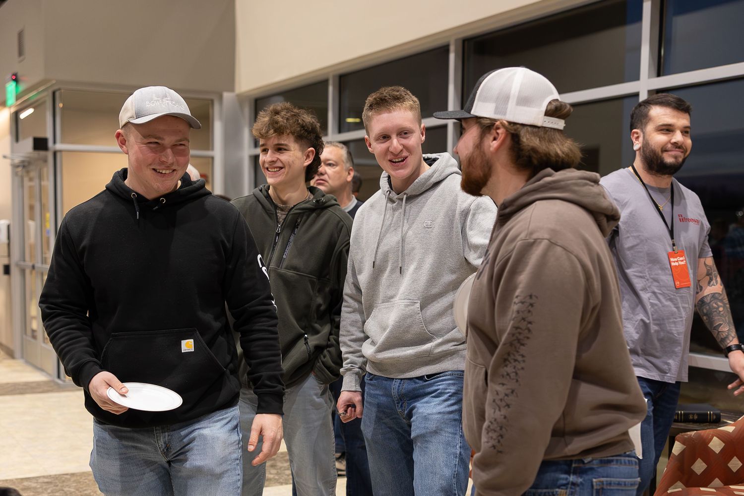 A group of people in casual attire gather and converse in a hallway setting.