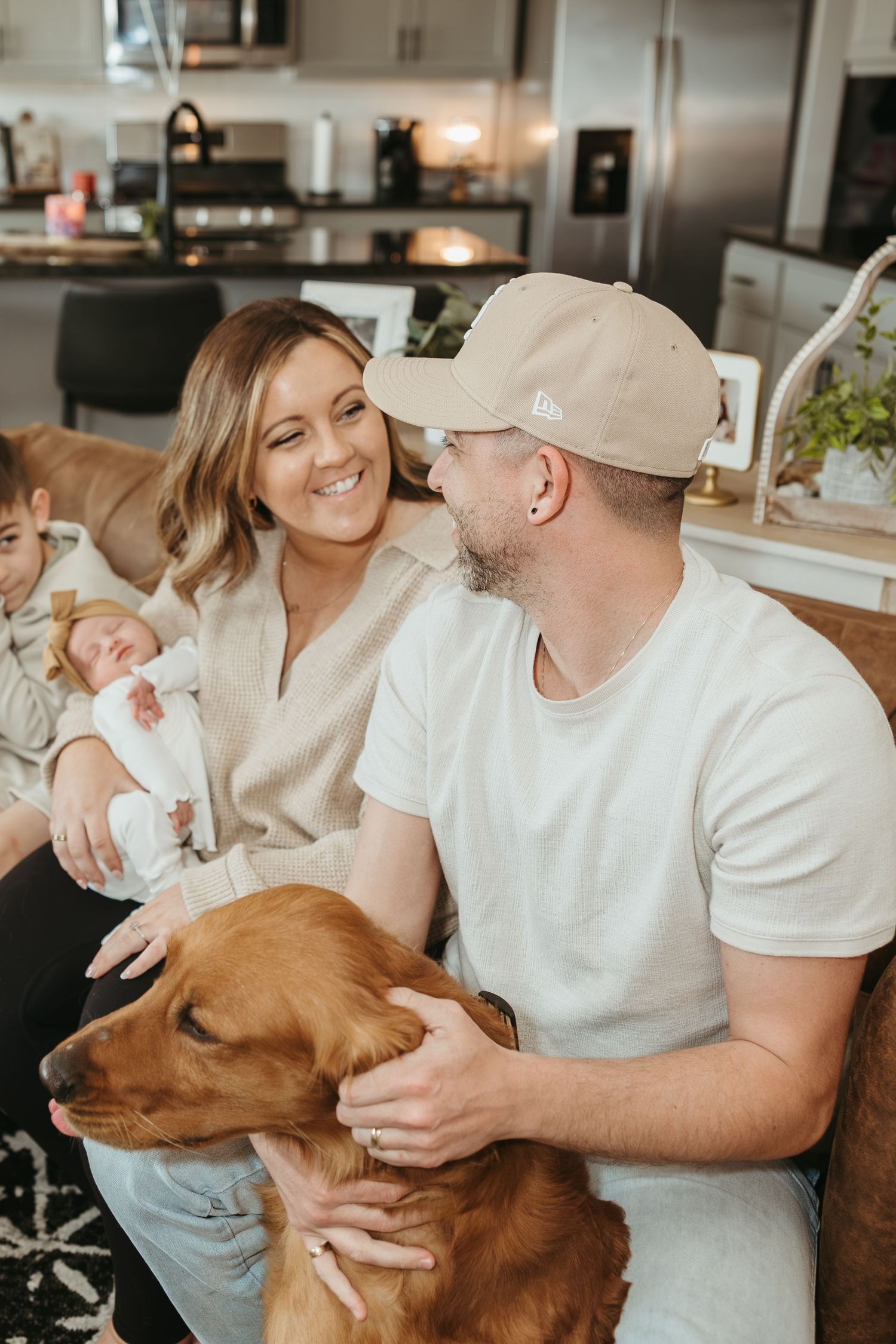 Happy couple relaxing in kitchen with their golden retriever and infant.
