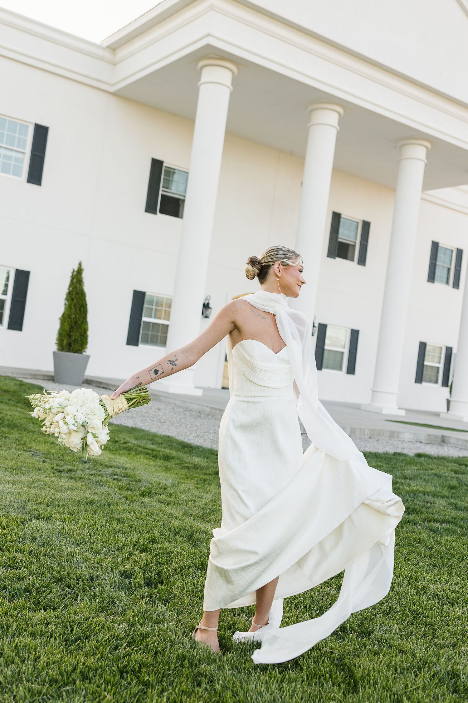 A person in a flowing white dress dances twirling on a grassy lawn in front of a white columned building.