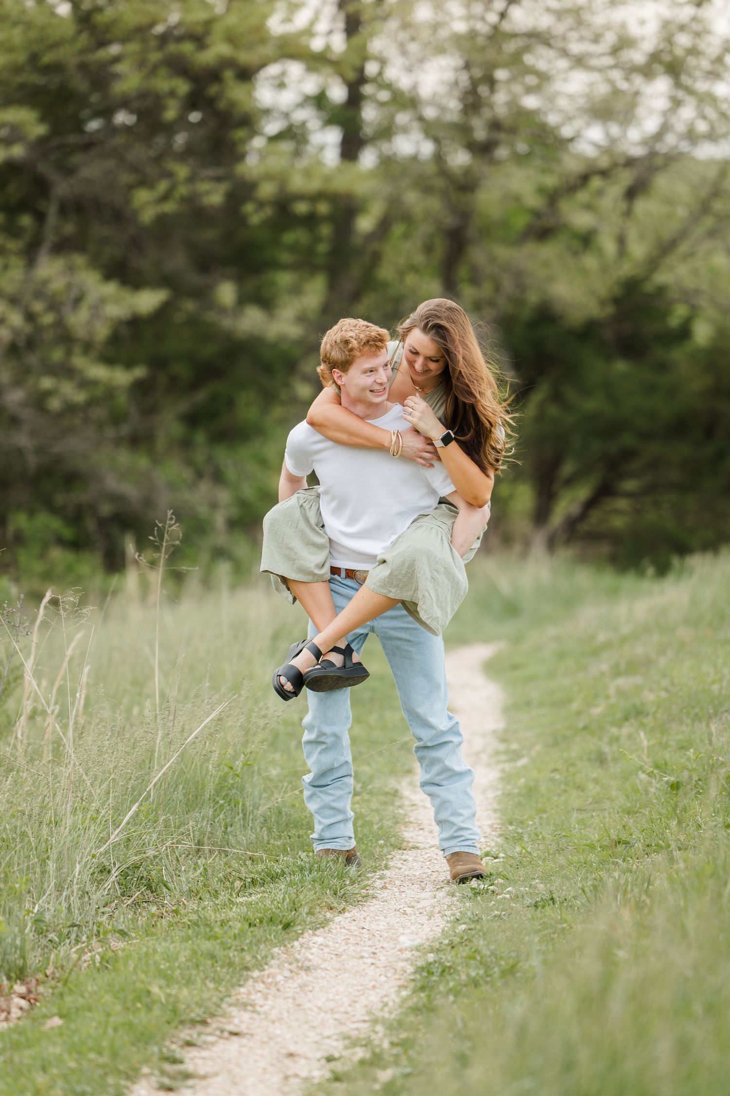 Two people sharing a joyful moment on a grassy hiking trail during a warm summer evening.
