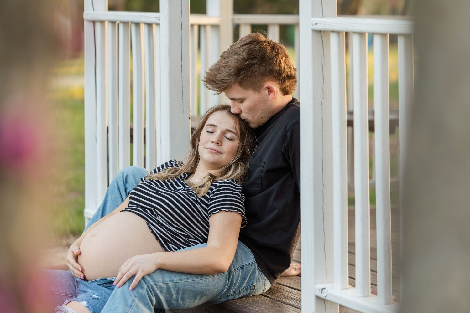 Expectant couple shares tender moment together on porch swing during maternity photoshoot.