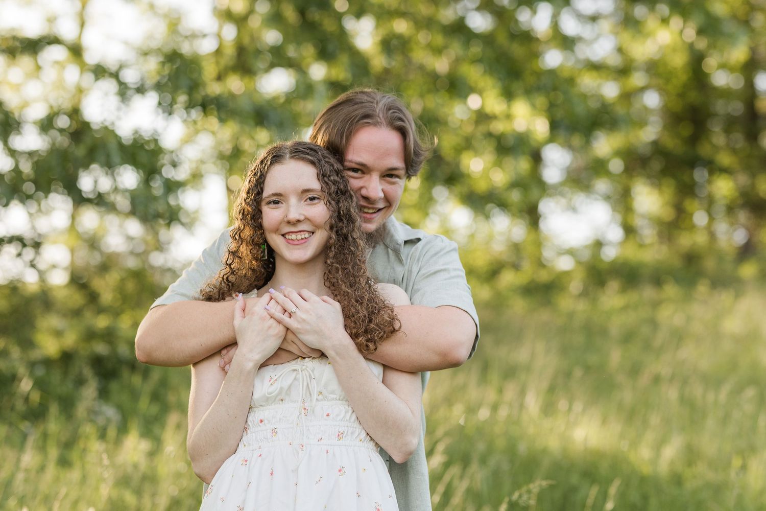 A romantic outdoor portrait against a sunlit natural backdrop of green grass and trees.