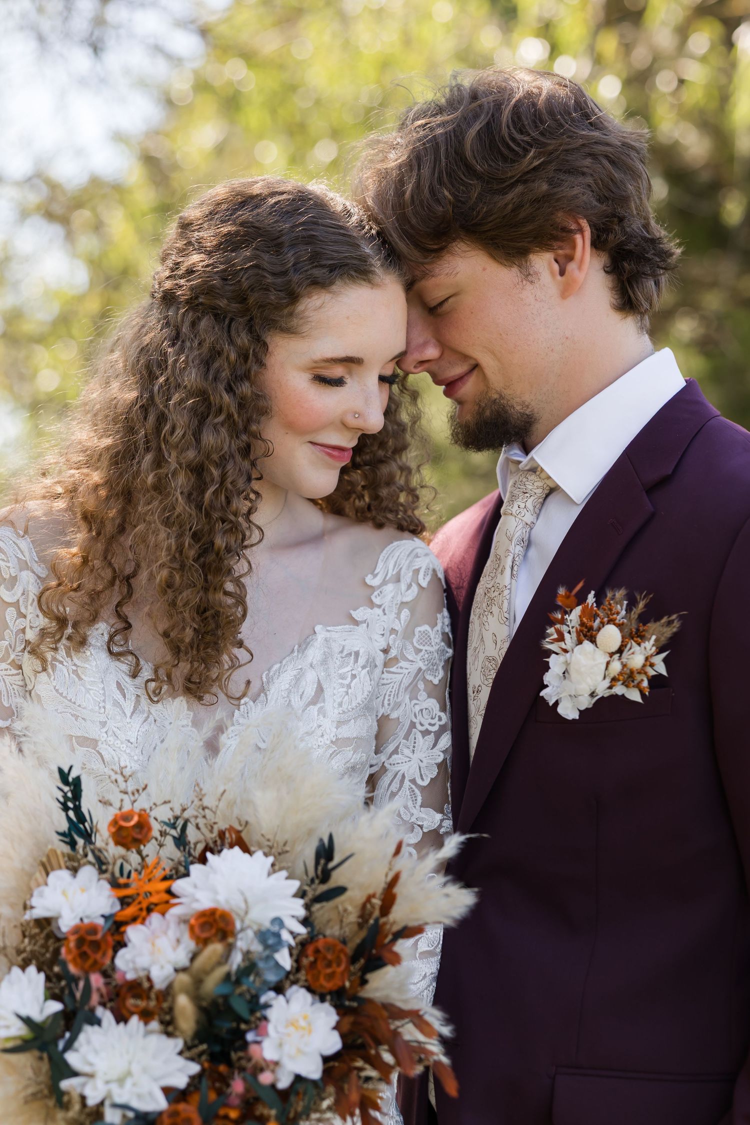 Bride and groom share a romantic forehead touch, she holds a boho bouquet with white dahlias and dried florals.