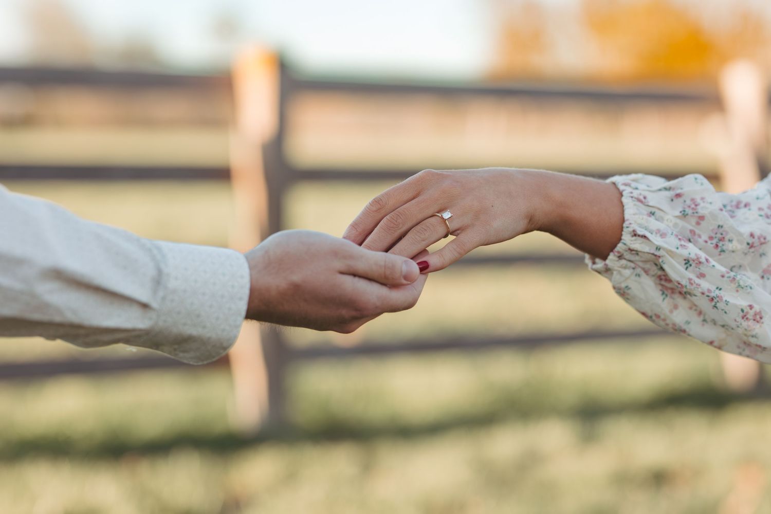 Close-up of hands exchanging wedding rings in golden sunset light.
