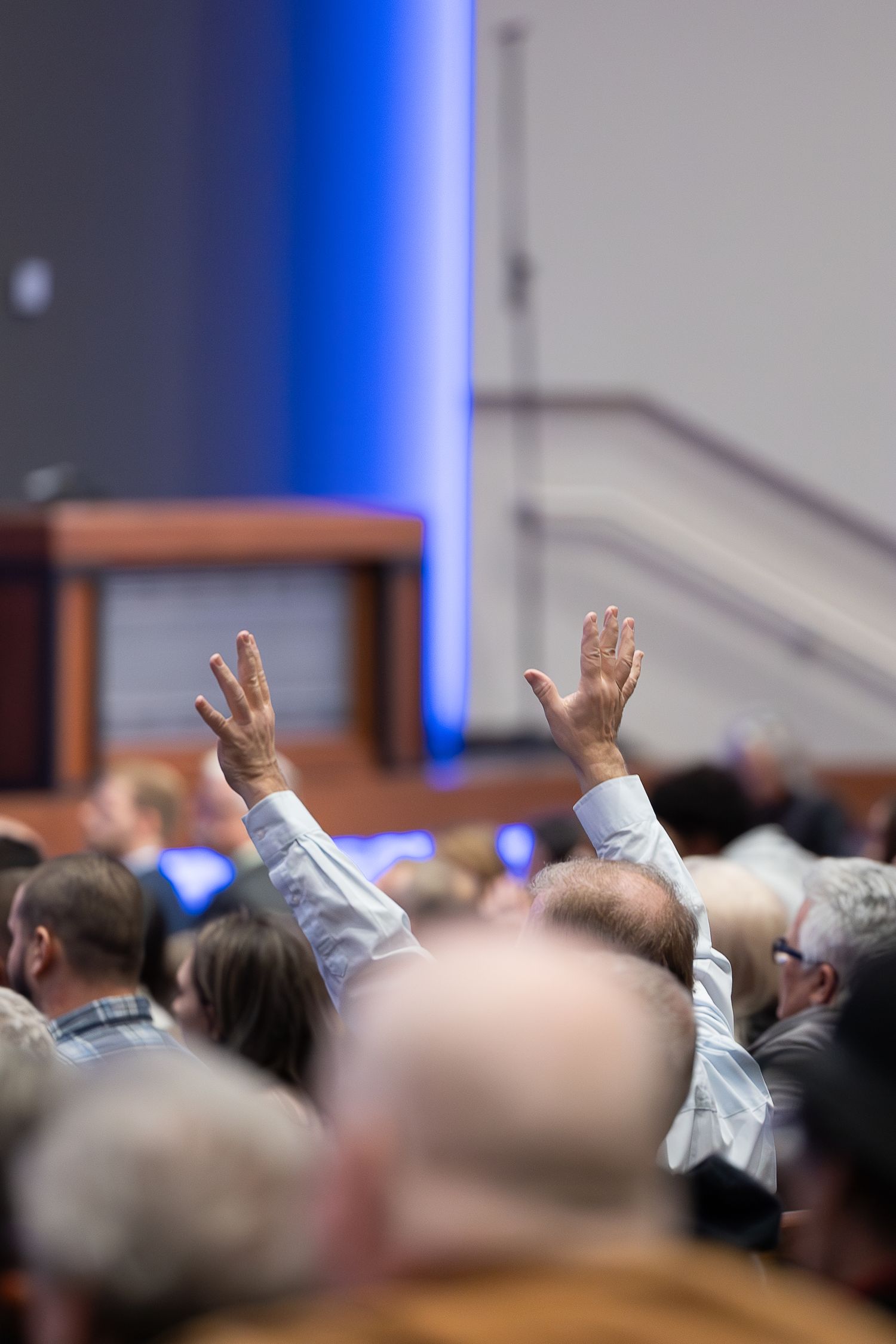 Raised hands during worship service visible among seated congregation members.