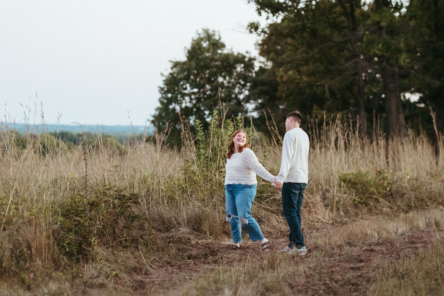 A couple takes a stroll together through a scenic hilltop meadow at dusk.