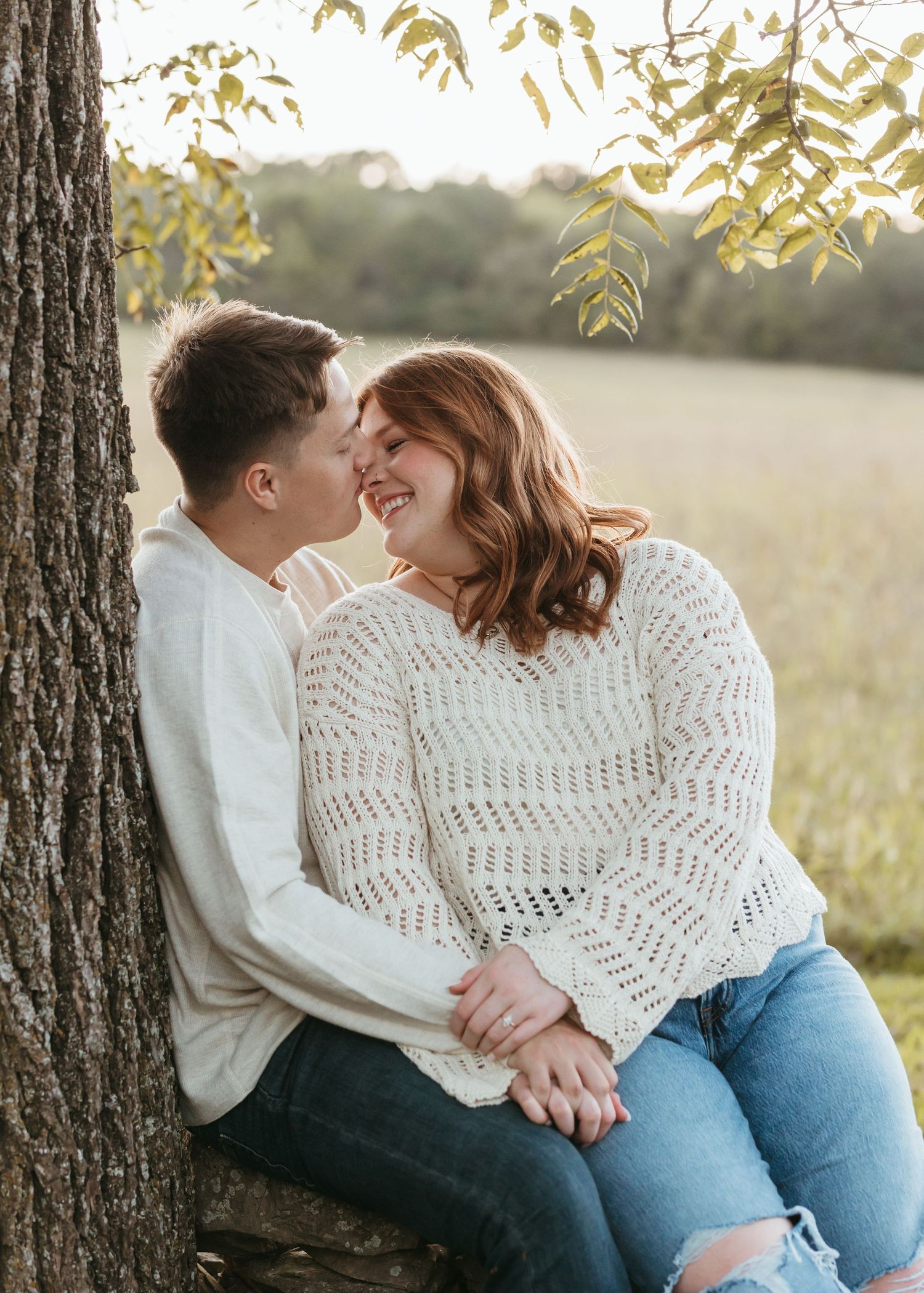 A couple shares a tender moment while sitting on a stone wall at sunset.