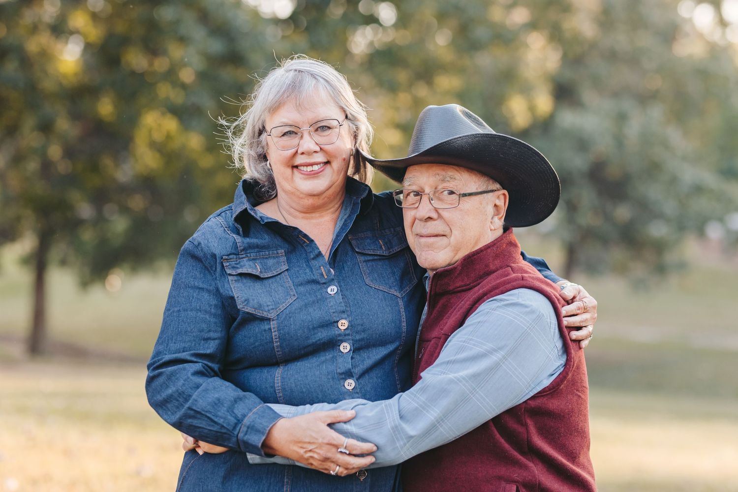 A senior couple in casual western wear shares an affectionate moment in an autumn setting.