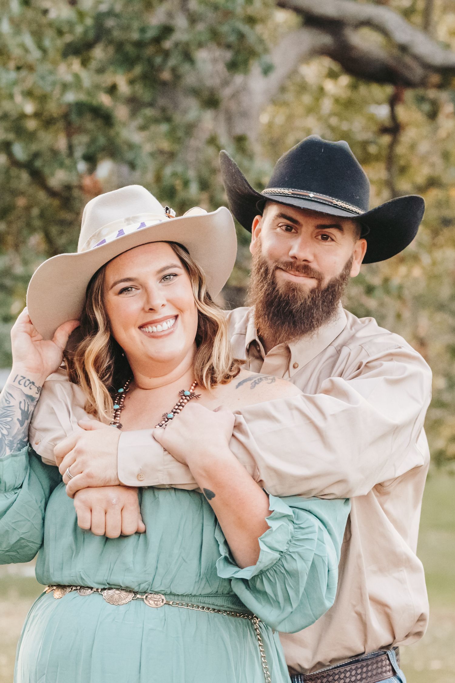 Western style couple wearing cowboy hats embrace in an outdoor autumn setting.