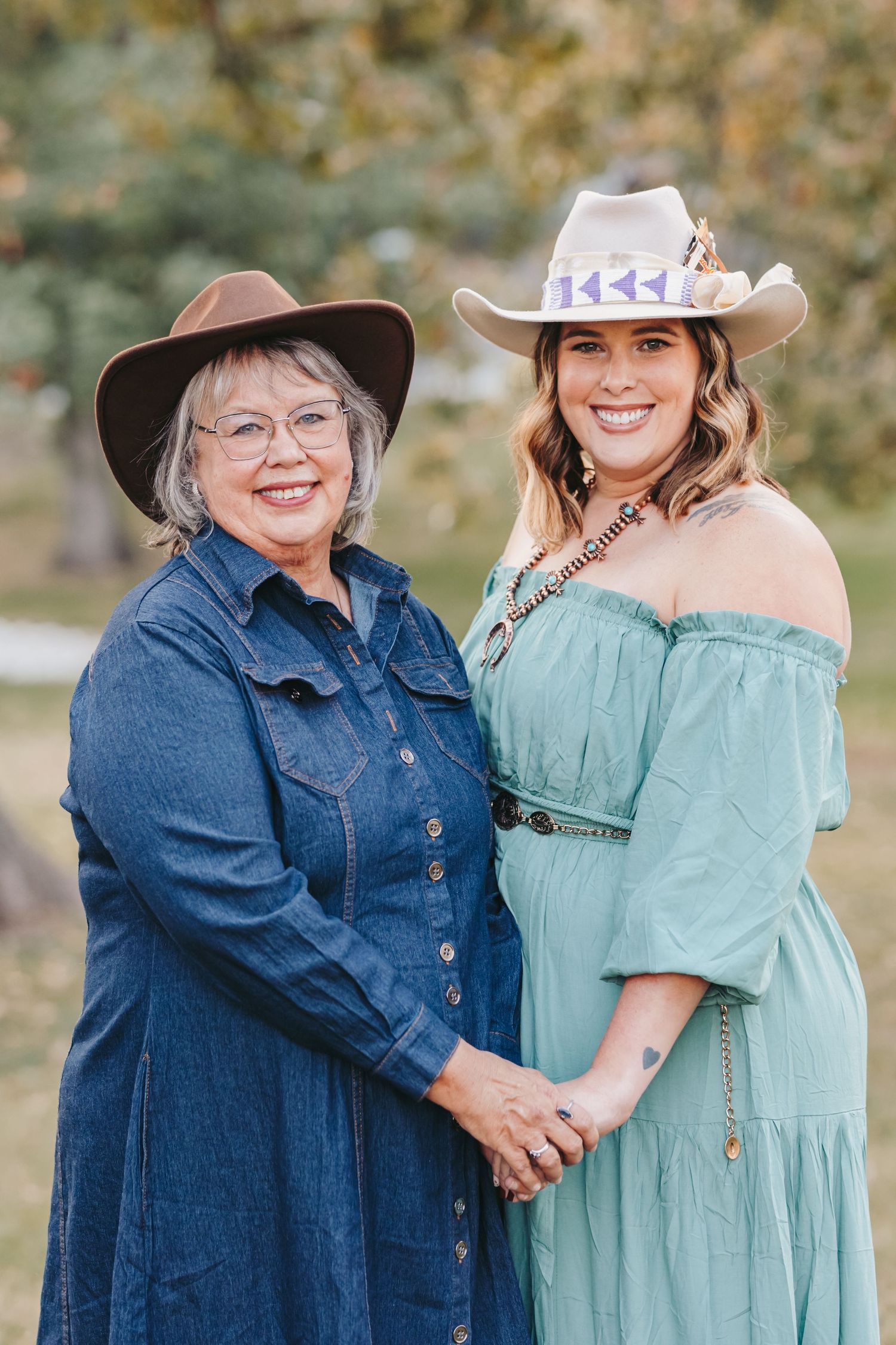Two people in western wear and cowboy hats pose together outdoors.