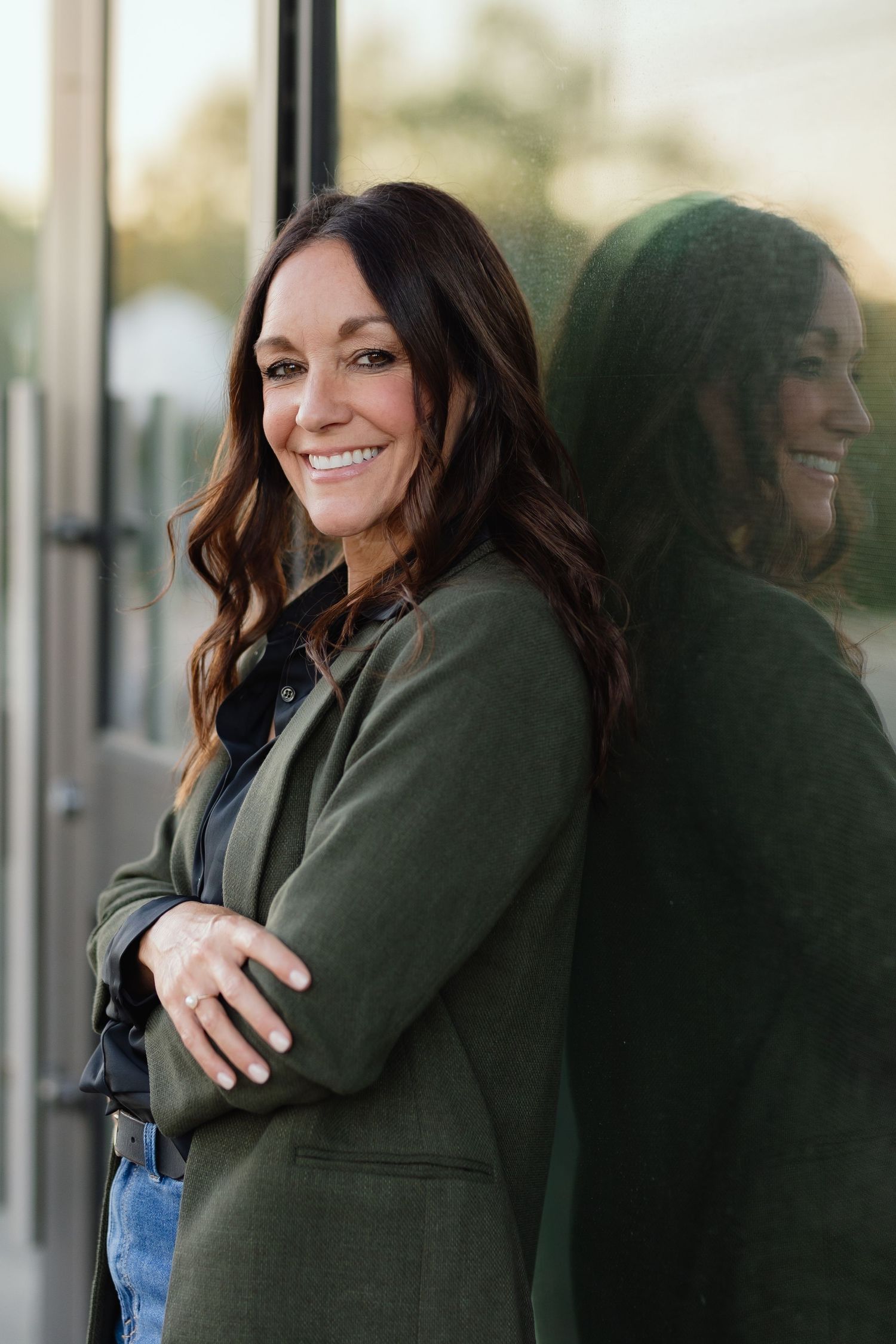 Stylish portrait showing reflection of person in olive blazer against glass window.