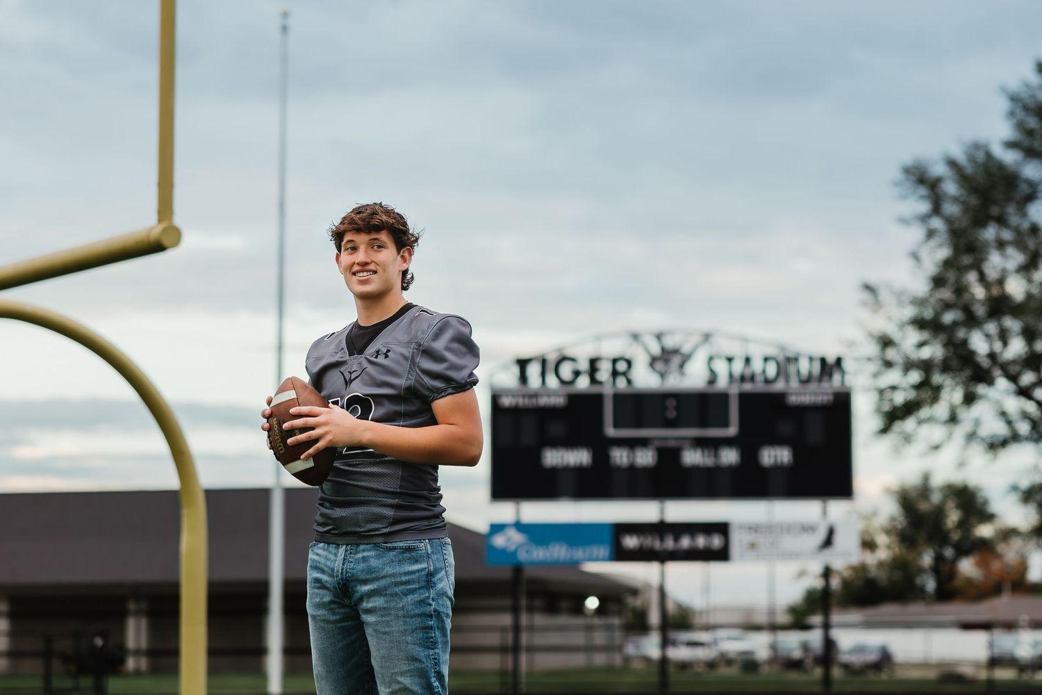 Athlete holds football while standing under Tiger Stadium scoreboard and goal post.