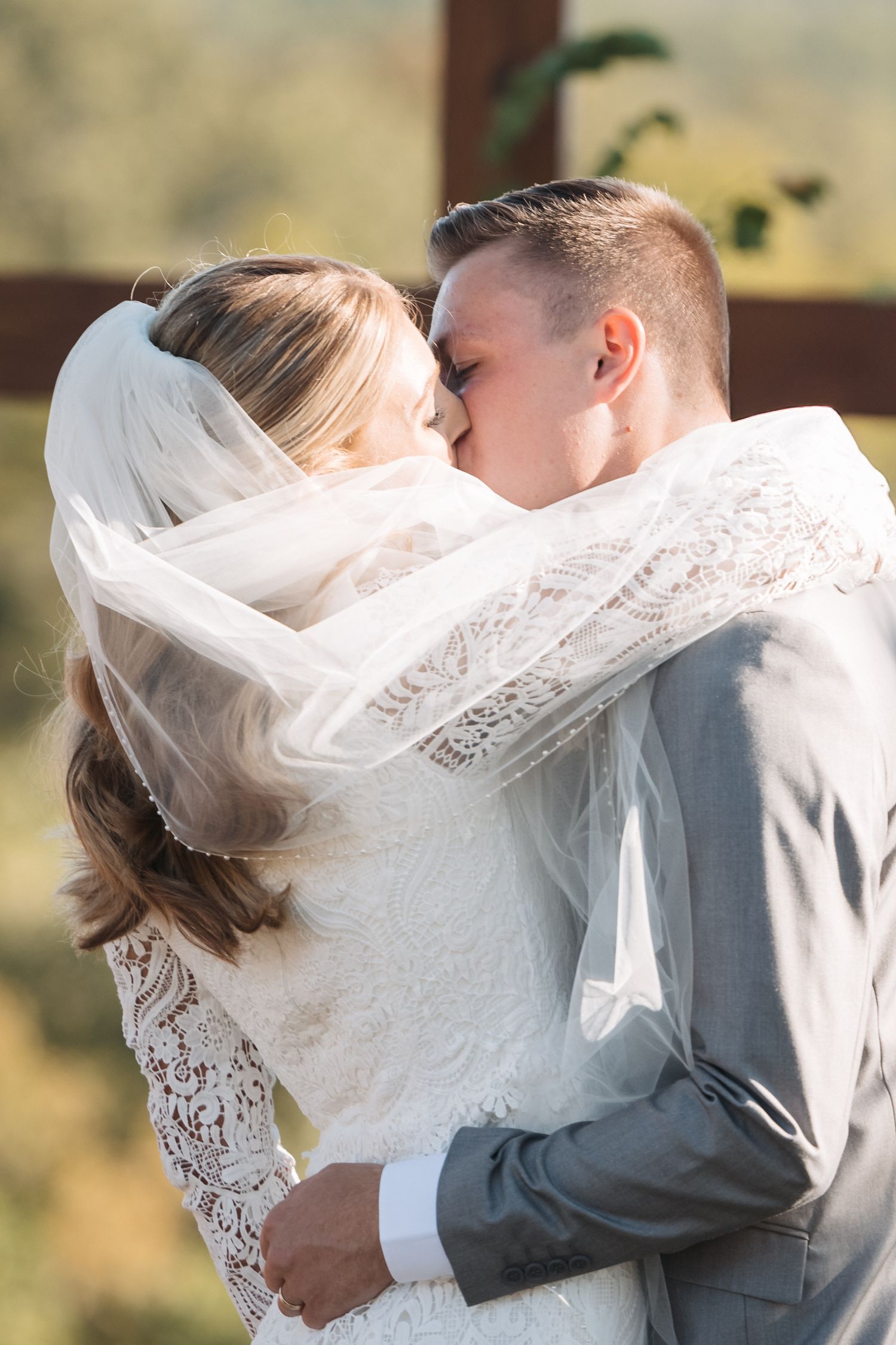Romantic wedding portrait of couple sharing kiss under flowing white veil.
