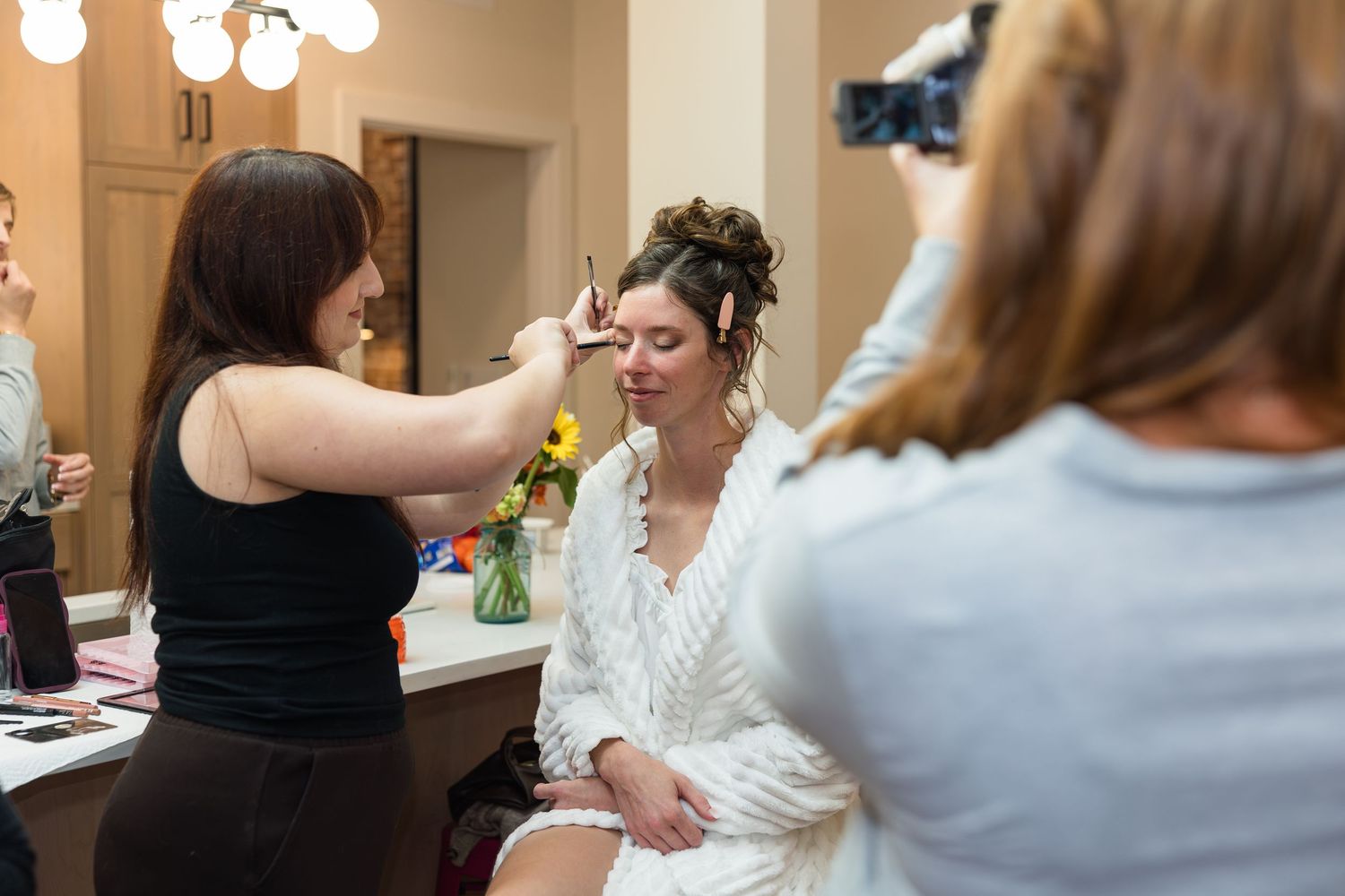 Bride getting hair and makeup done by stylist in dressing room mirror before wedding ceremony.