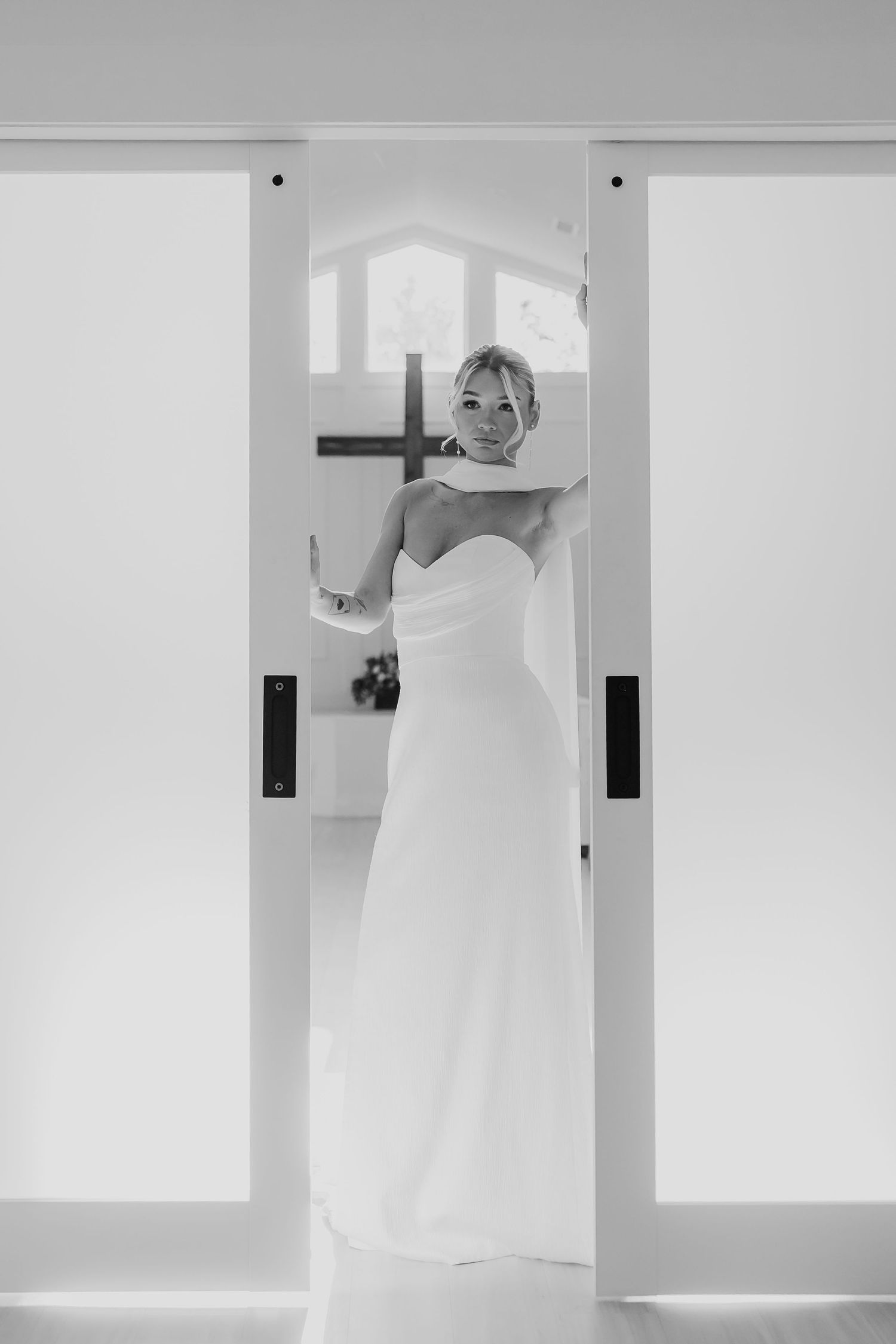 Black and white portrait of a bride in a strapless white gown standing in an elegant doorway.