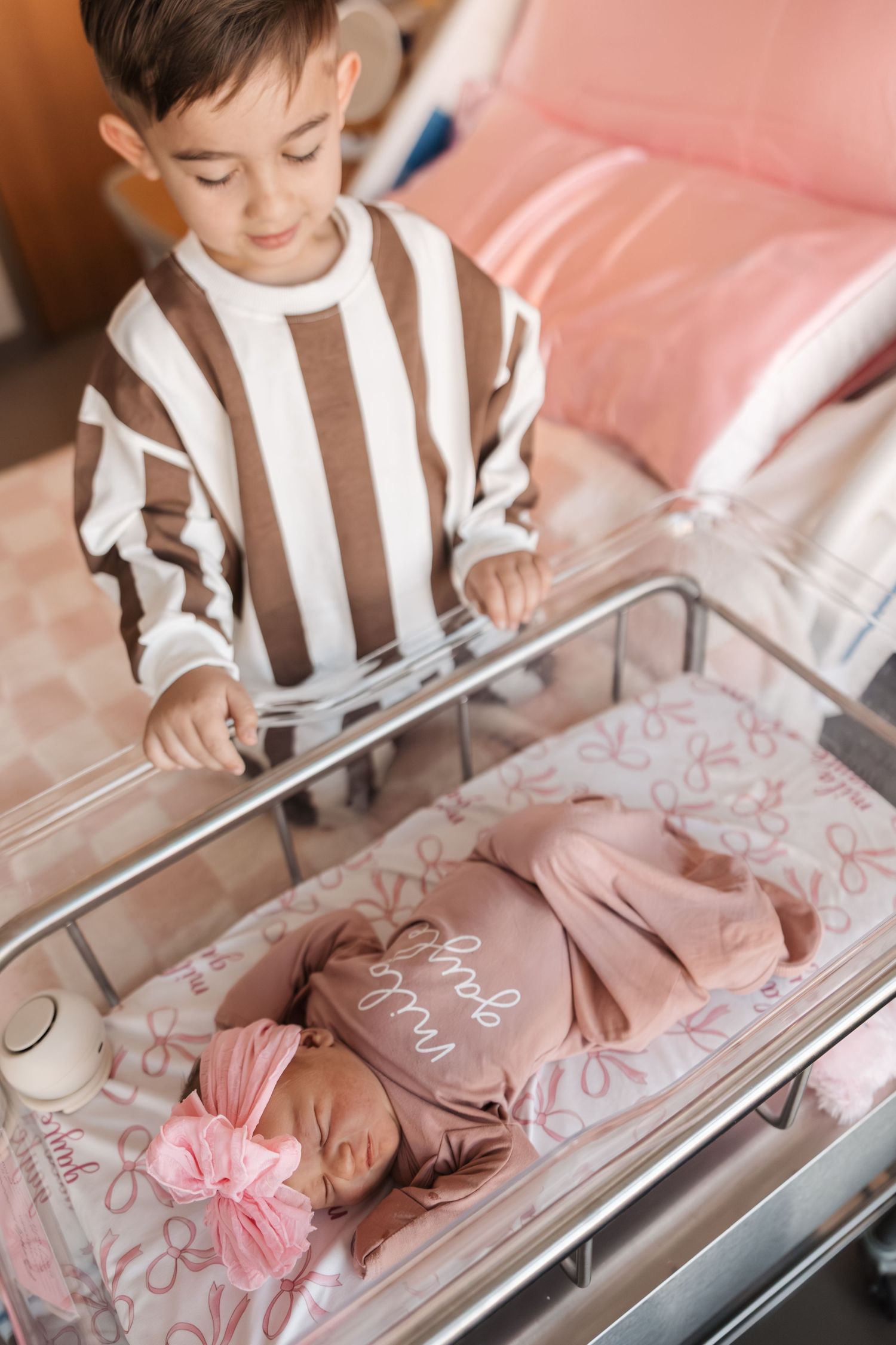 A newborn baby sleeps peacefully in a hospital bassinet while being gently observed from above.