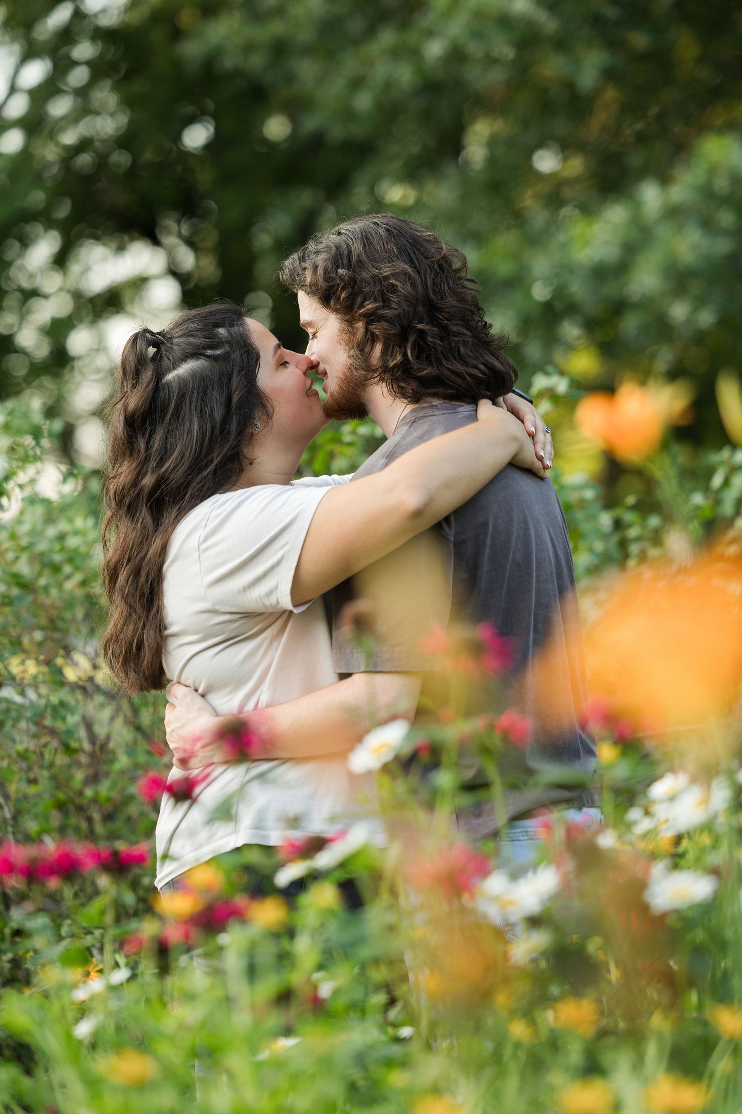 A romantic couple shares an intimate moment among colorful summer flowers in a garden.