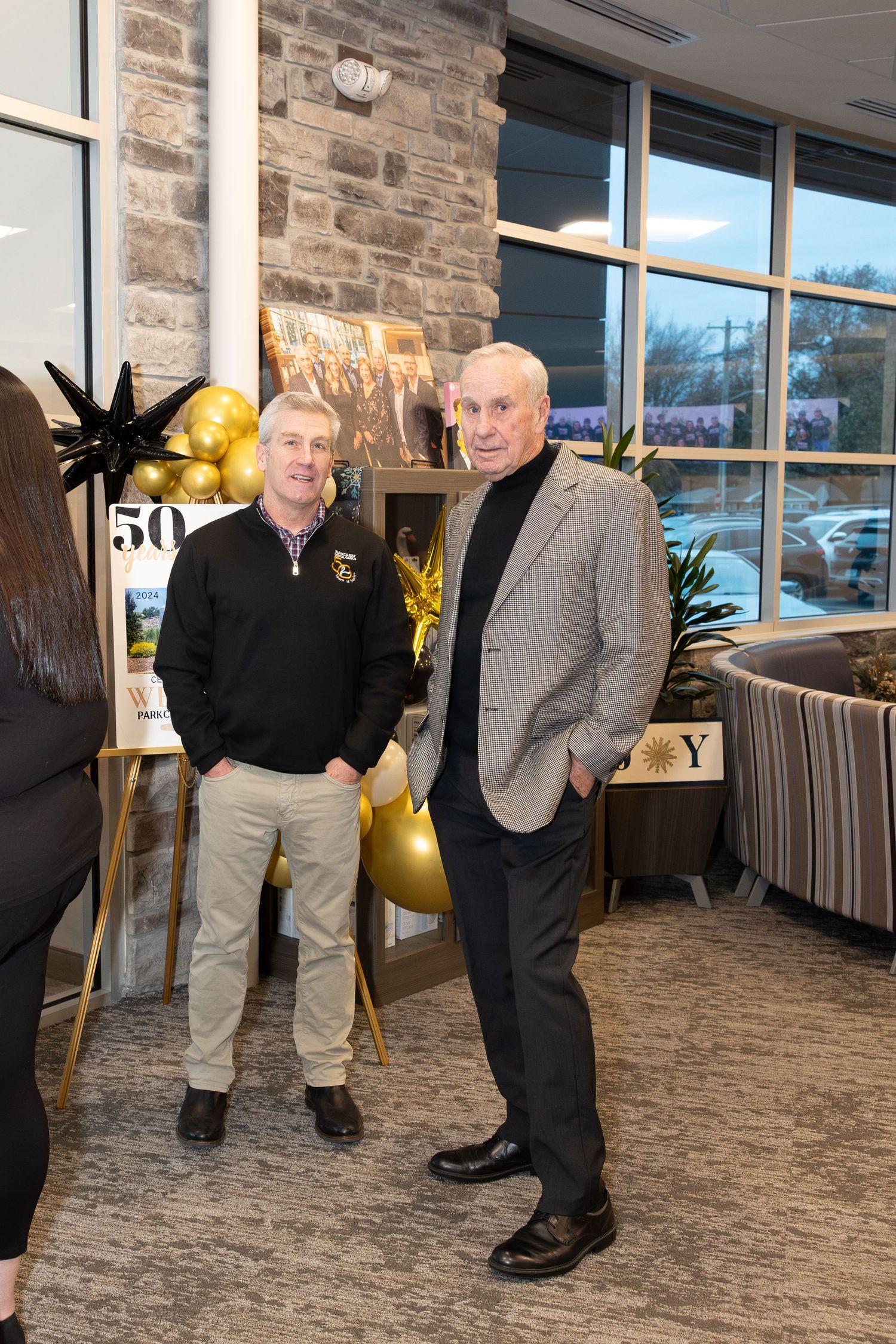 Two men in business casual attire stand chatting at corporate event with decorative backdrop.