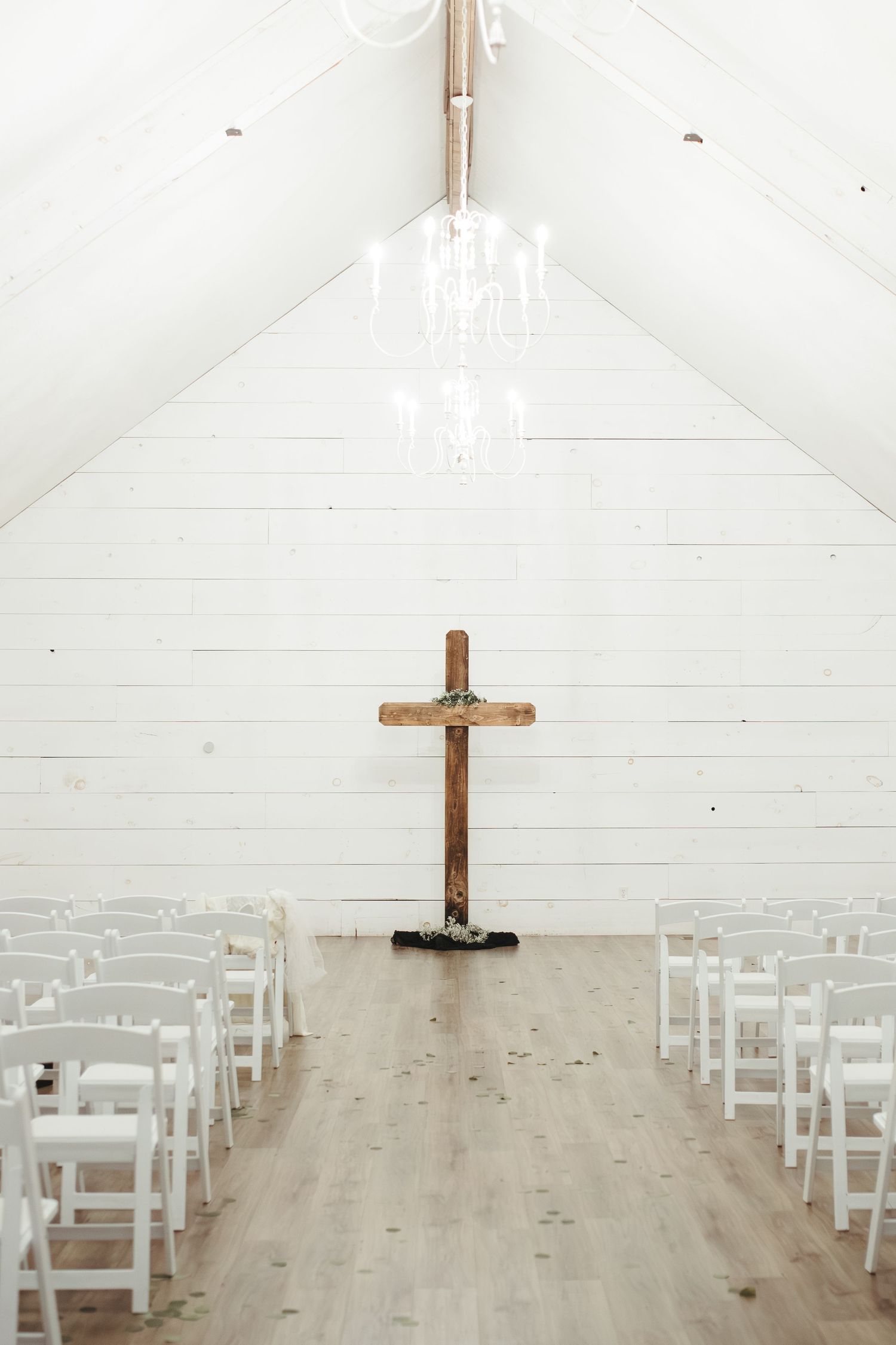 Minimalist white chapel interior with wooden cross and white chairs lined up for ceremony.