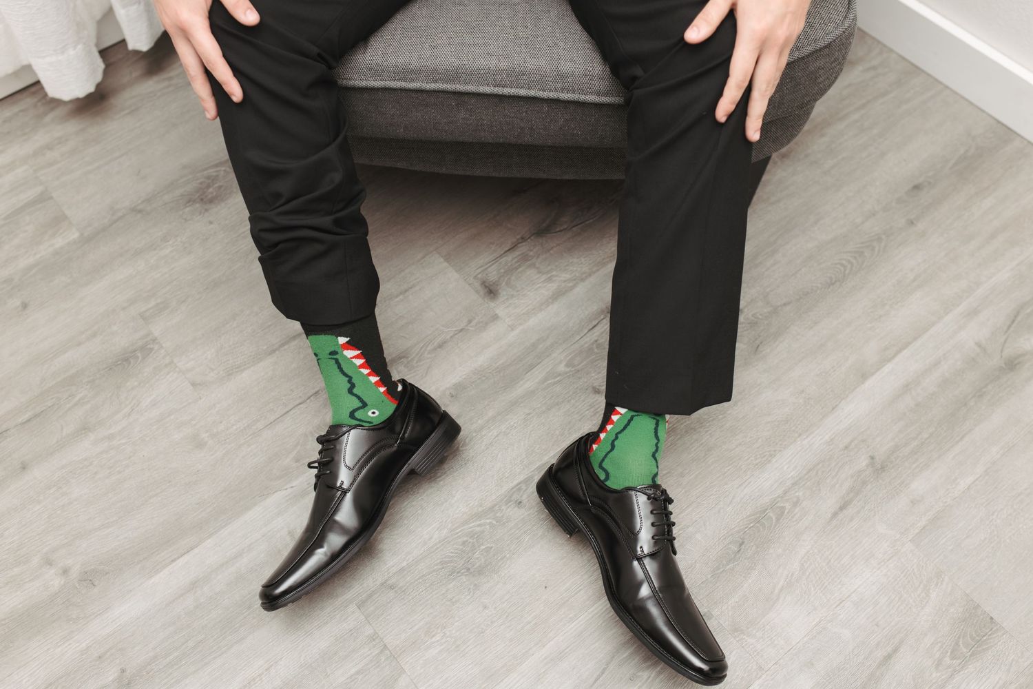 Green patterned socks peek out between black dress shoes and pants on gray floor.