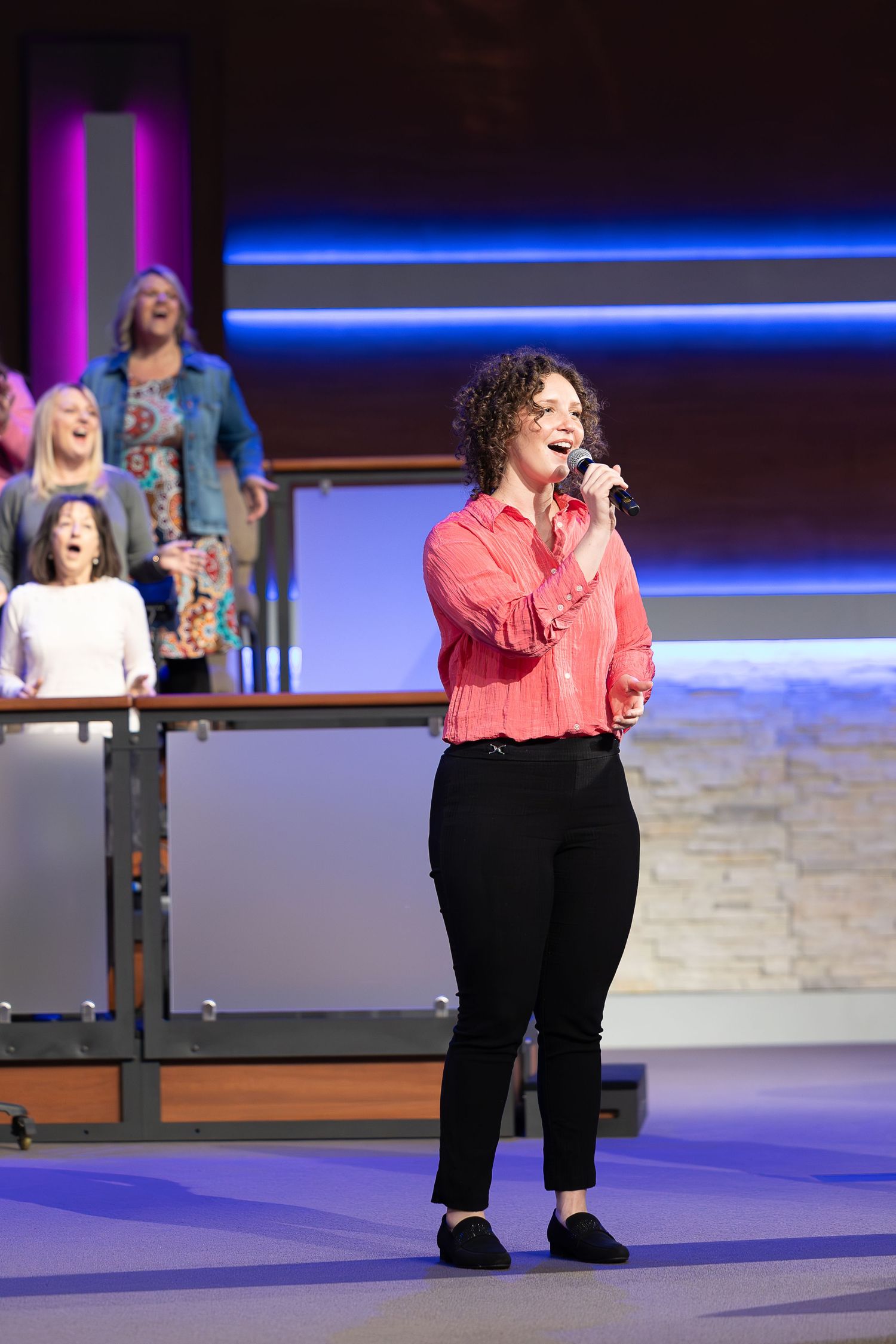 A performer in a red top singing on stage during a worship service.
