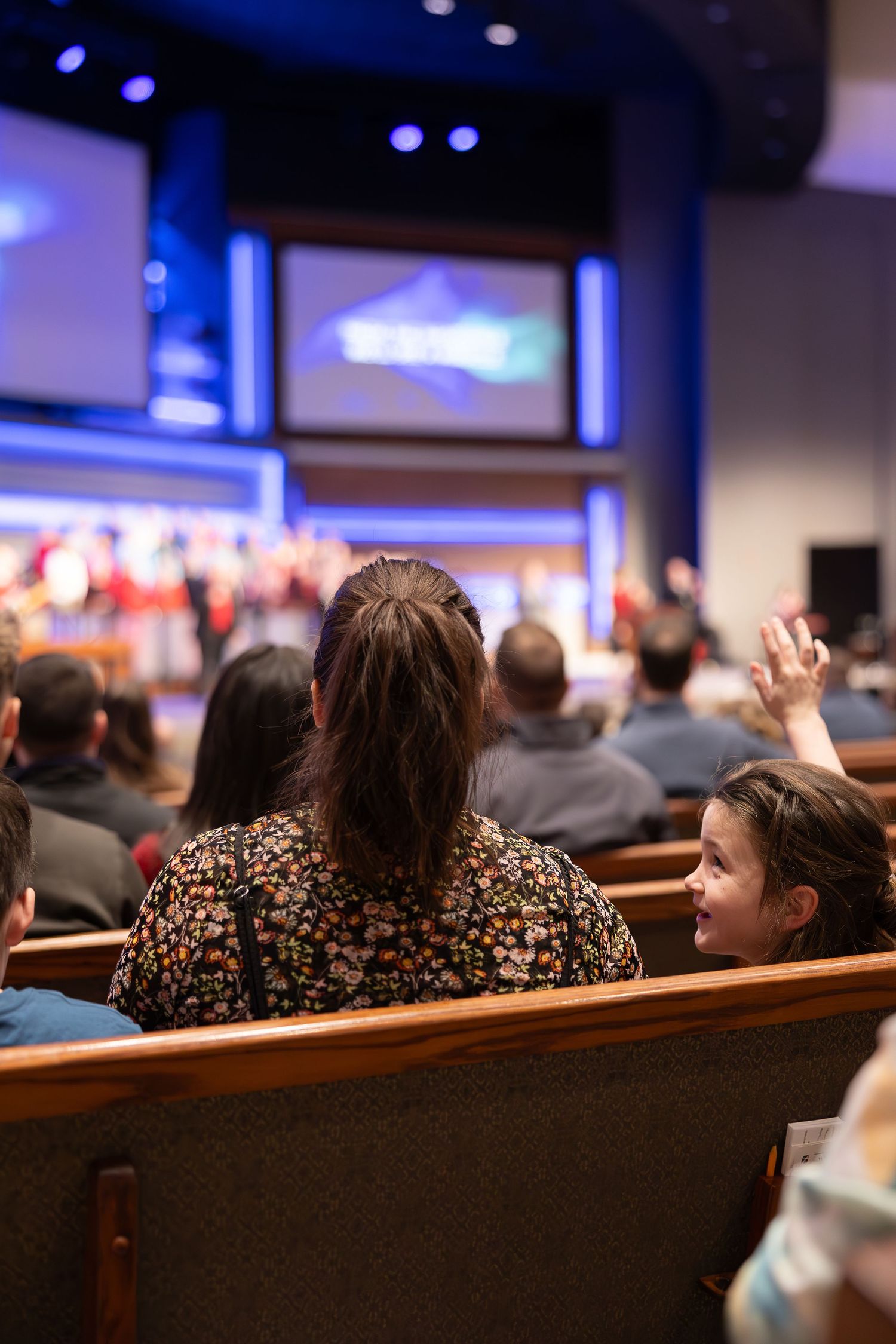Church attendees watching service with screens displaying glowing cross in background.