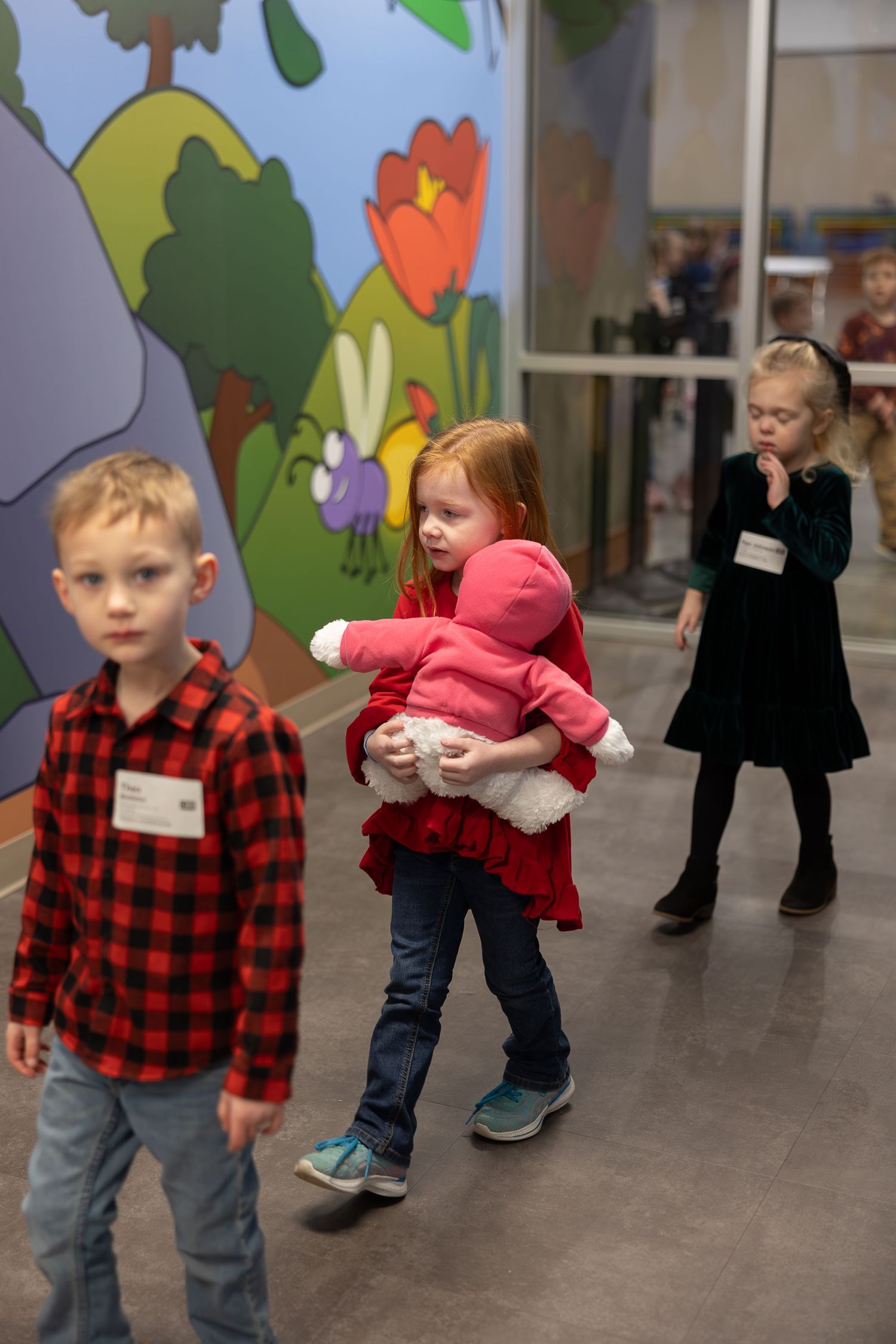 Children participate in indoor activities against a colorful wall mural featuring flowers and trees in a classroom setting.