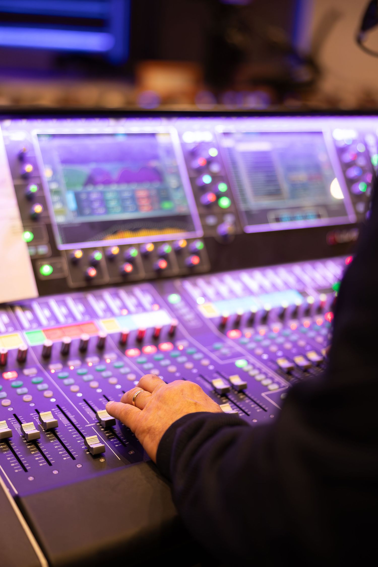 Close-up of audio mixing board faders with purple backlighting.