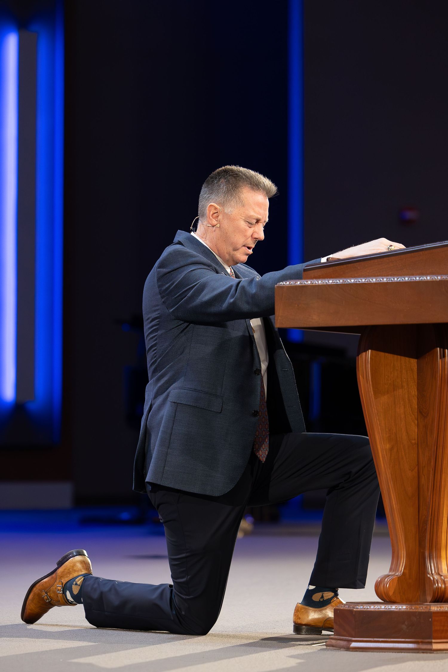 Person kneeling at wooden podium during prayer in church sanctuary.