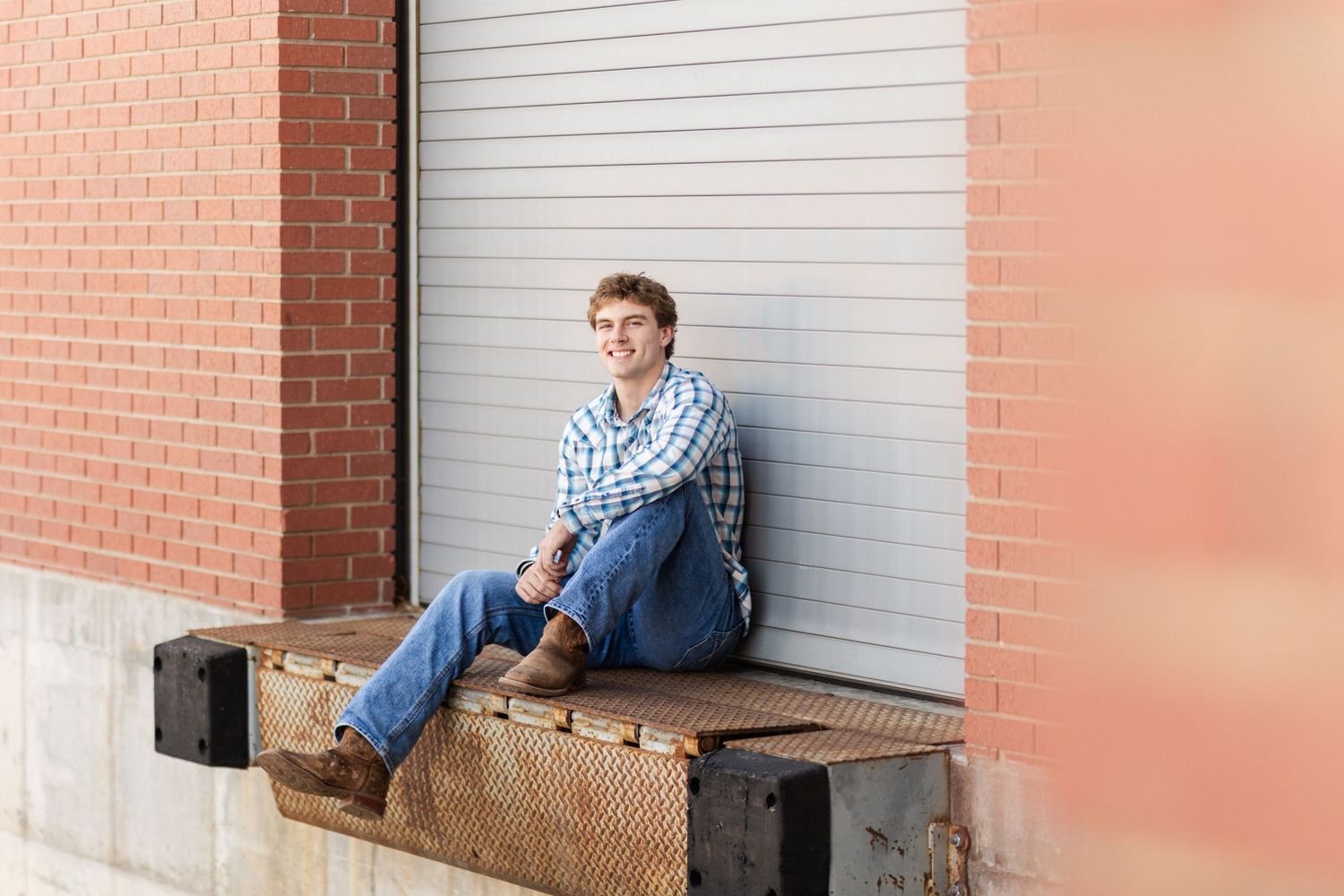 Relaxed pose on loading dock against brick wall and metal door.