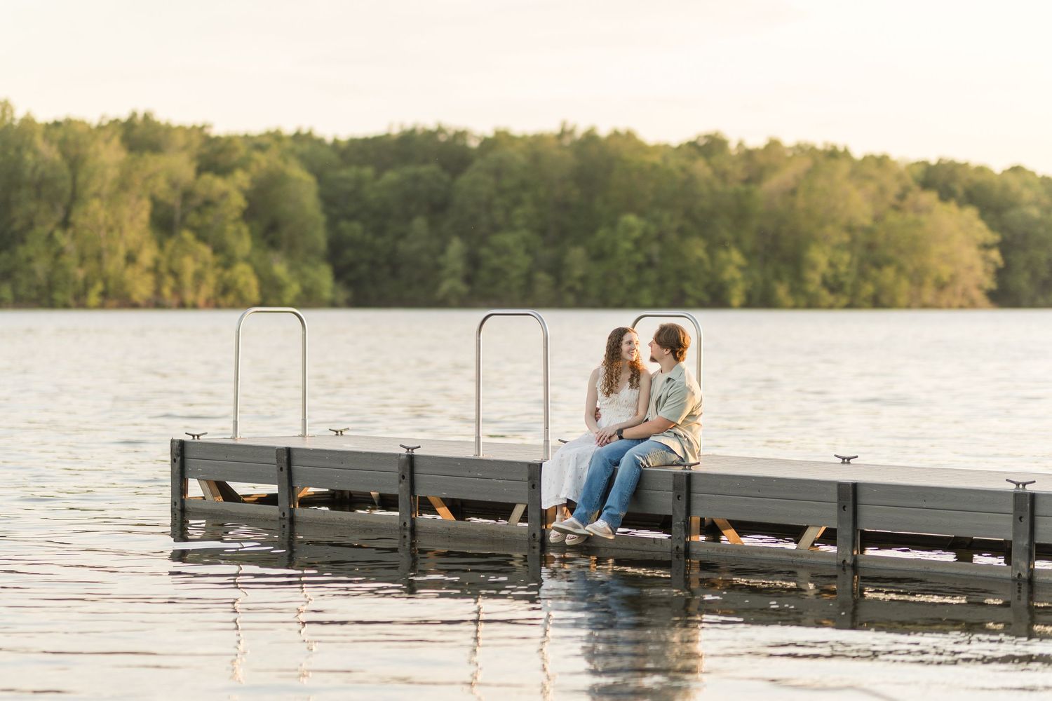 People relaxing on a wooden dock at sunset beside a tranquil lake surrounded by autumn trees.