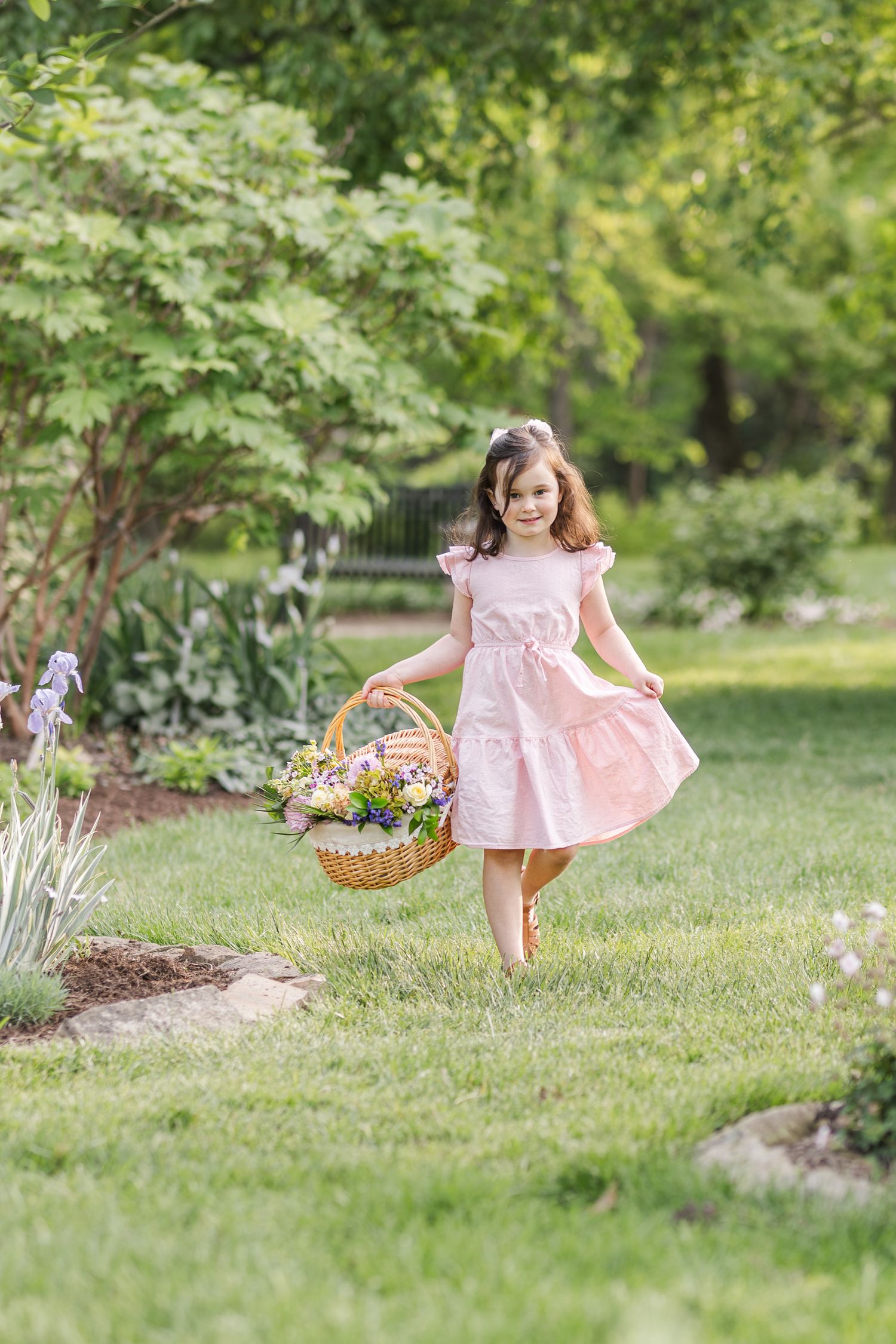 Young girl in pink dress runs through garden with flowers basket during bright spring afternoon.