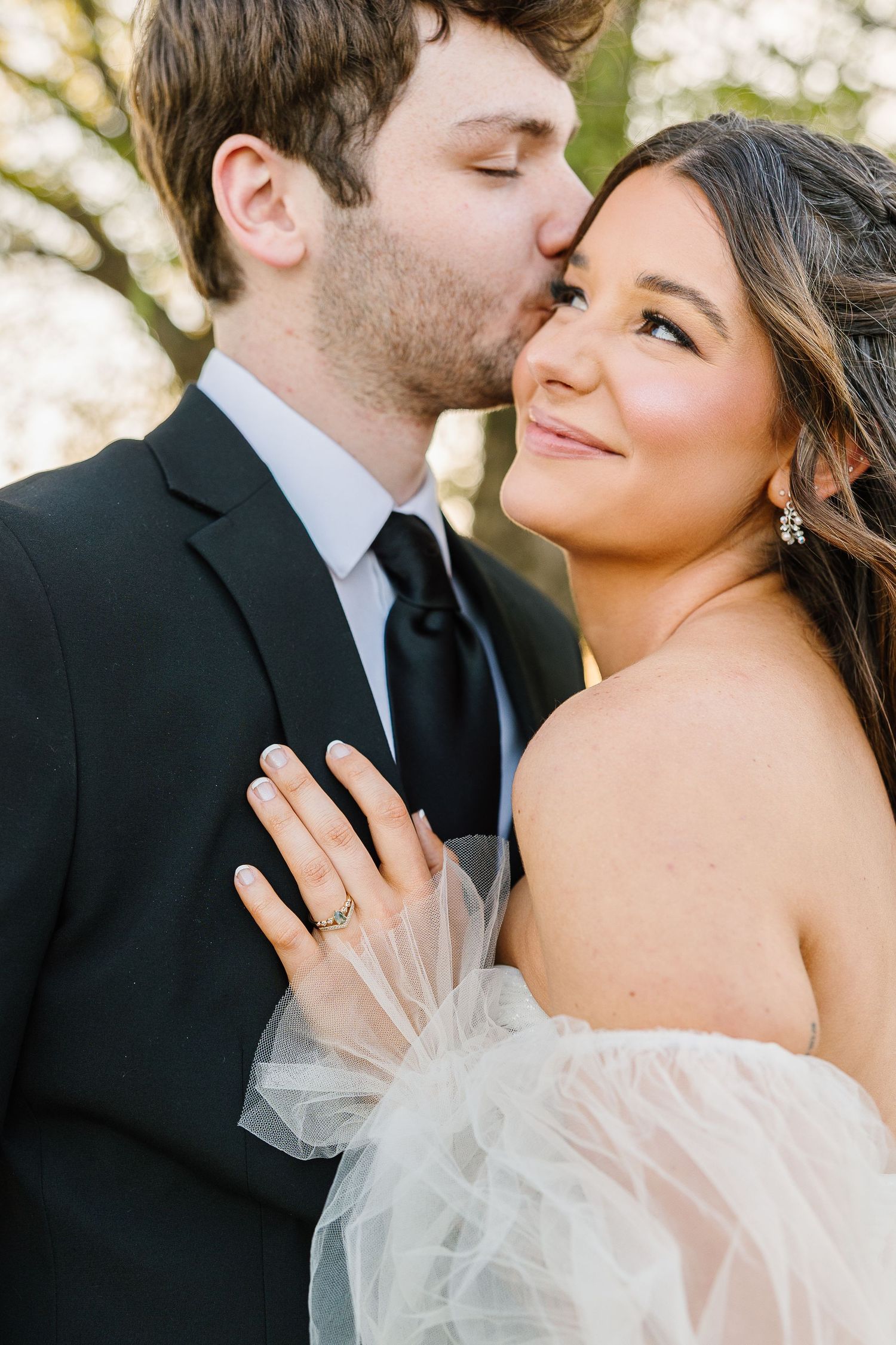 A romantic wedding portrait showing a tender moment between newlyweds with soft natural lighting in the background.