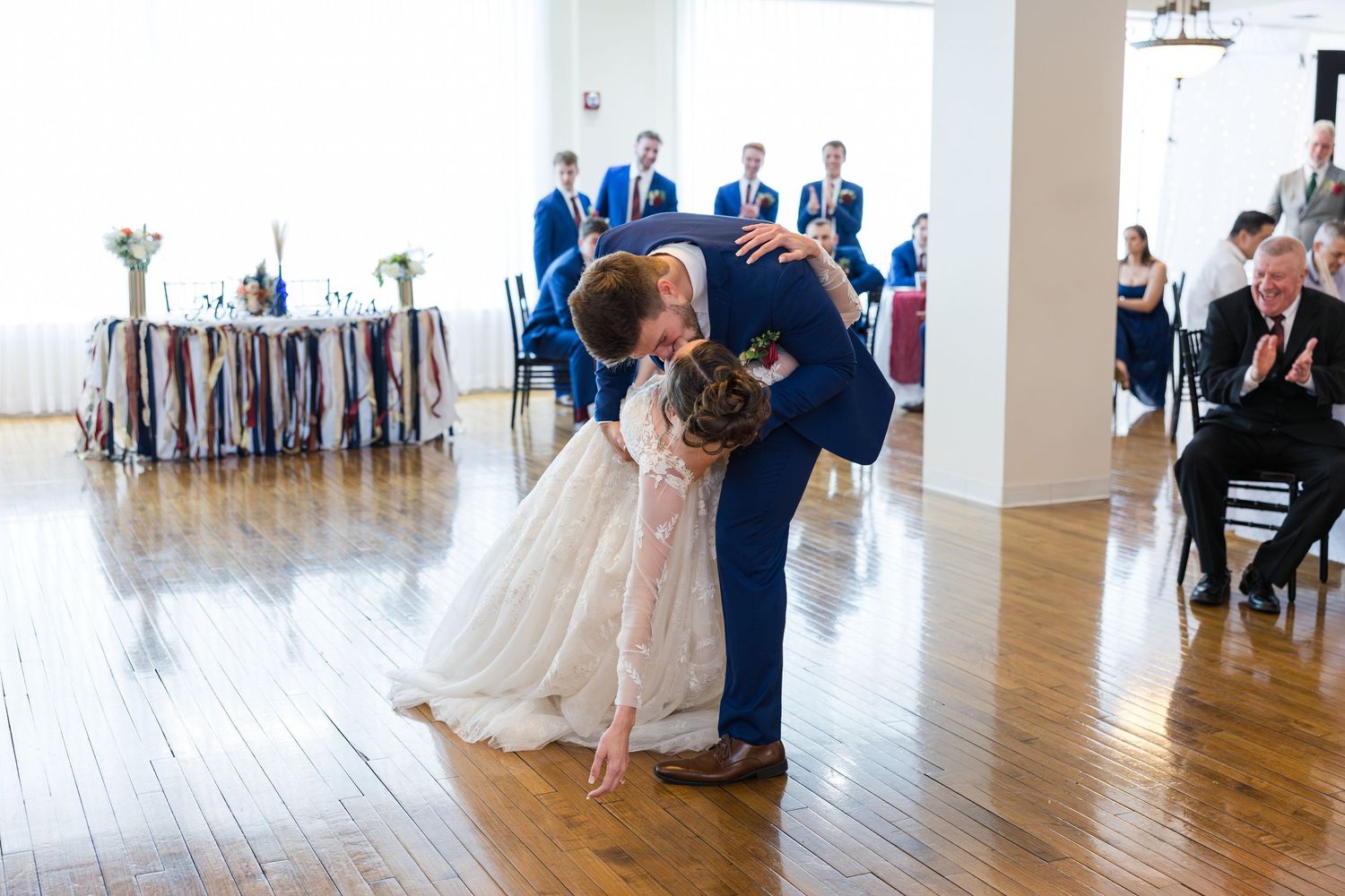 Newlyweds share romantic dip kiss during first dance at elegant wedding reception venue.