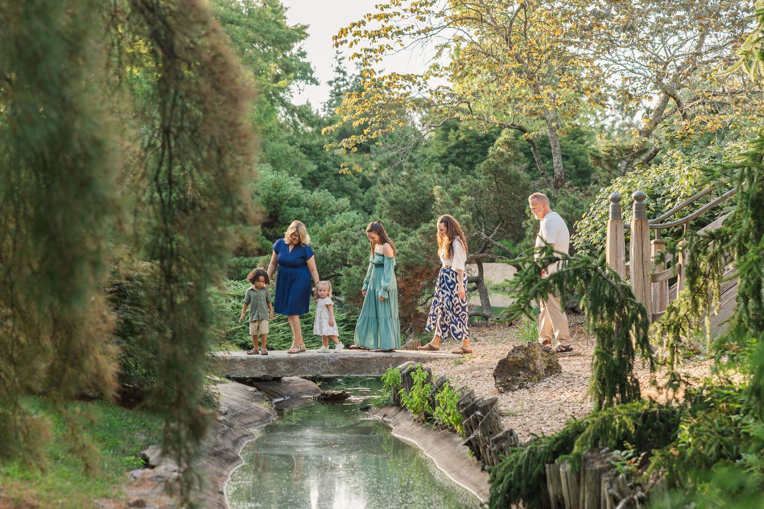 Family gathering on a stone bridge in a lush garden with a serene pond below.