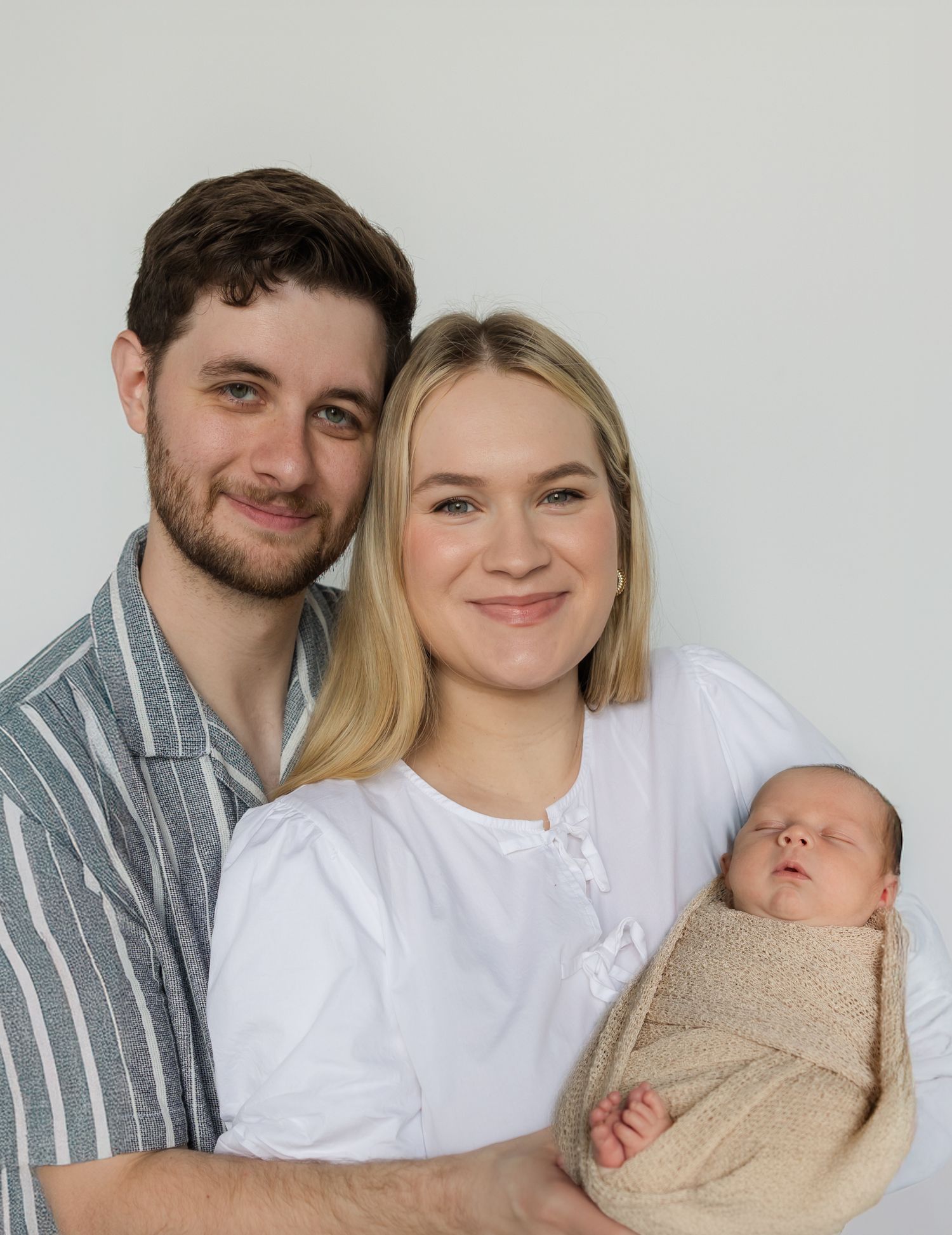 A couple poses together in a series of five intimate photos showing their growing family with a newborn baby.