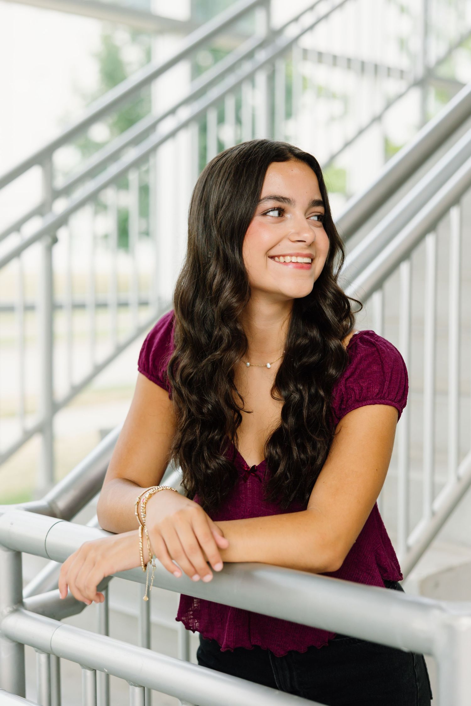 Person in burgundy top leans against metal railing while smiling in indoor professional photography session.