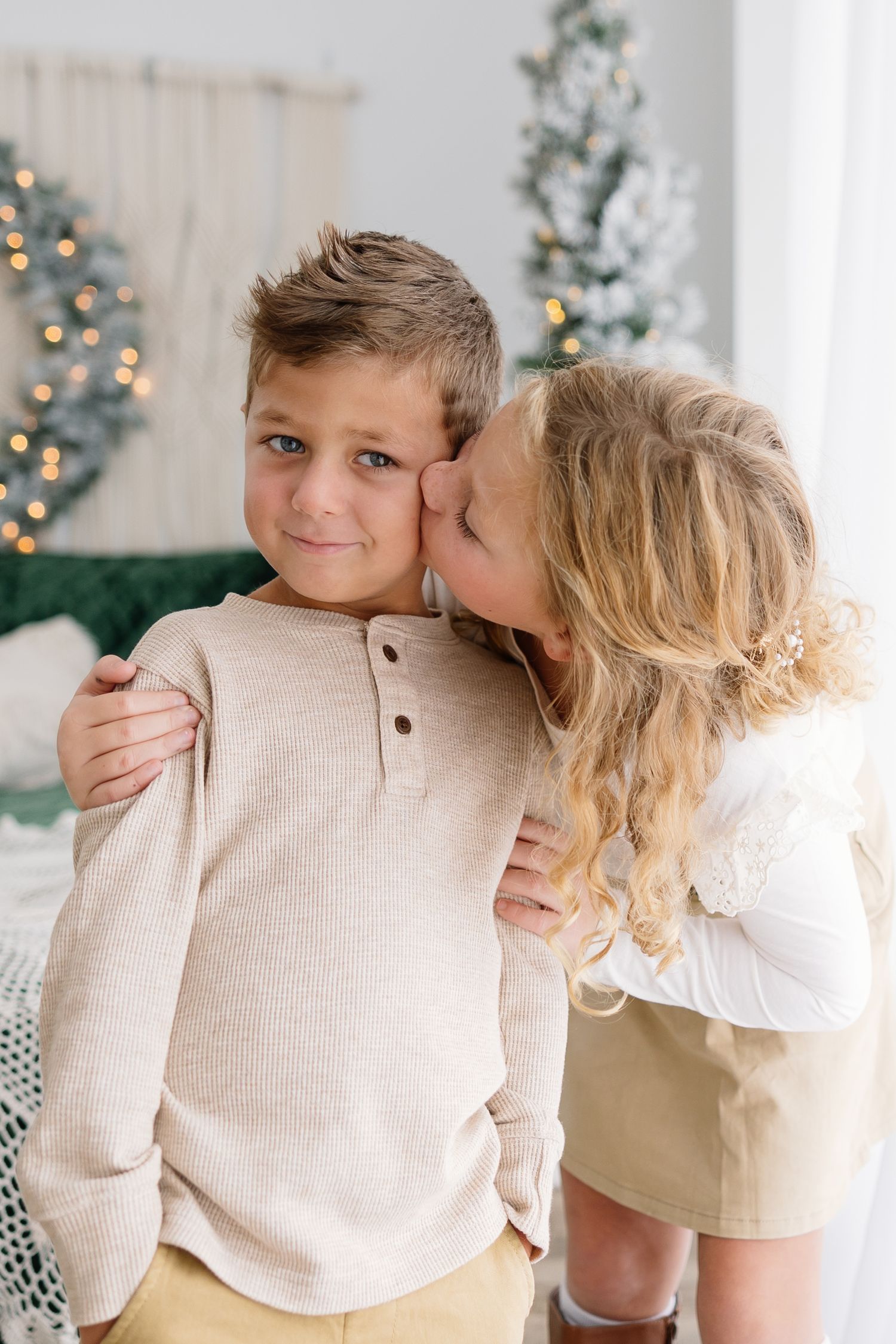 A sweet moment between two children with a decorated Christmas tree in the background.