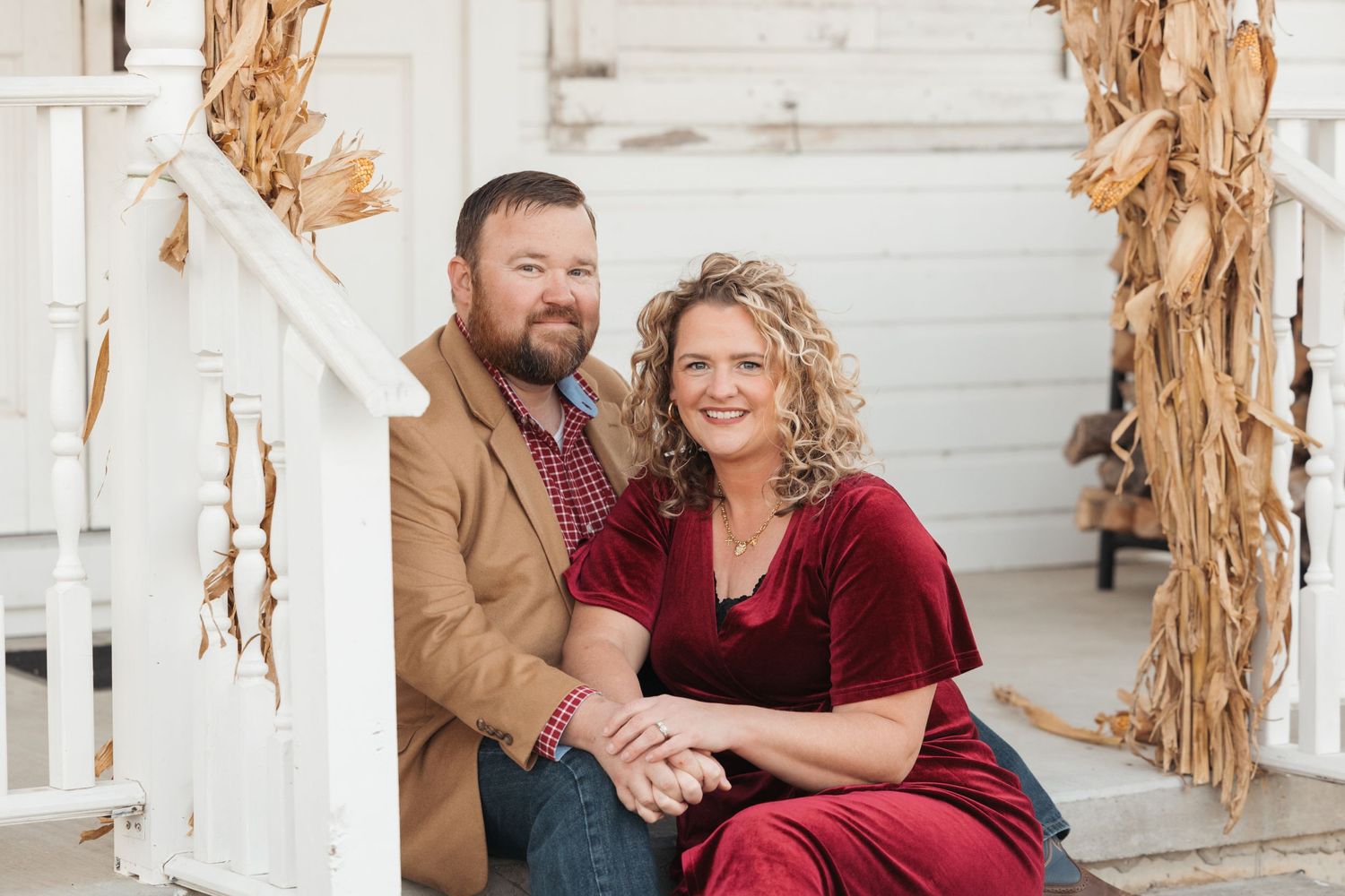 Happy couple sitting together on white porch with autumn decorations.