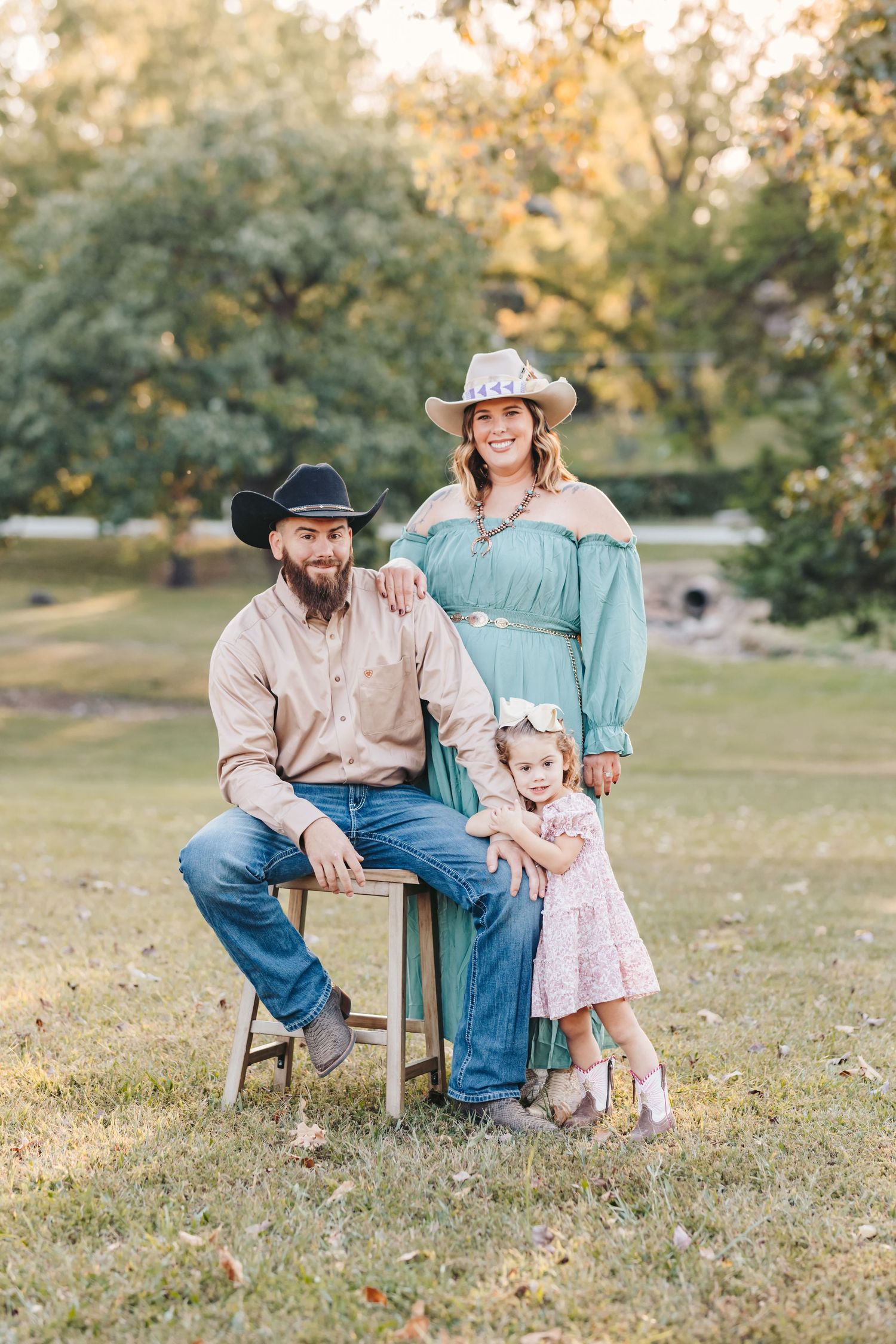 Family in western wear poses on wooden stool during outdoor photo session.