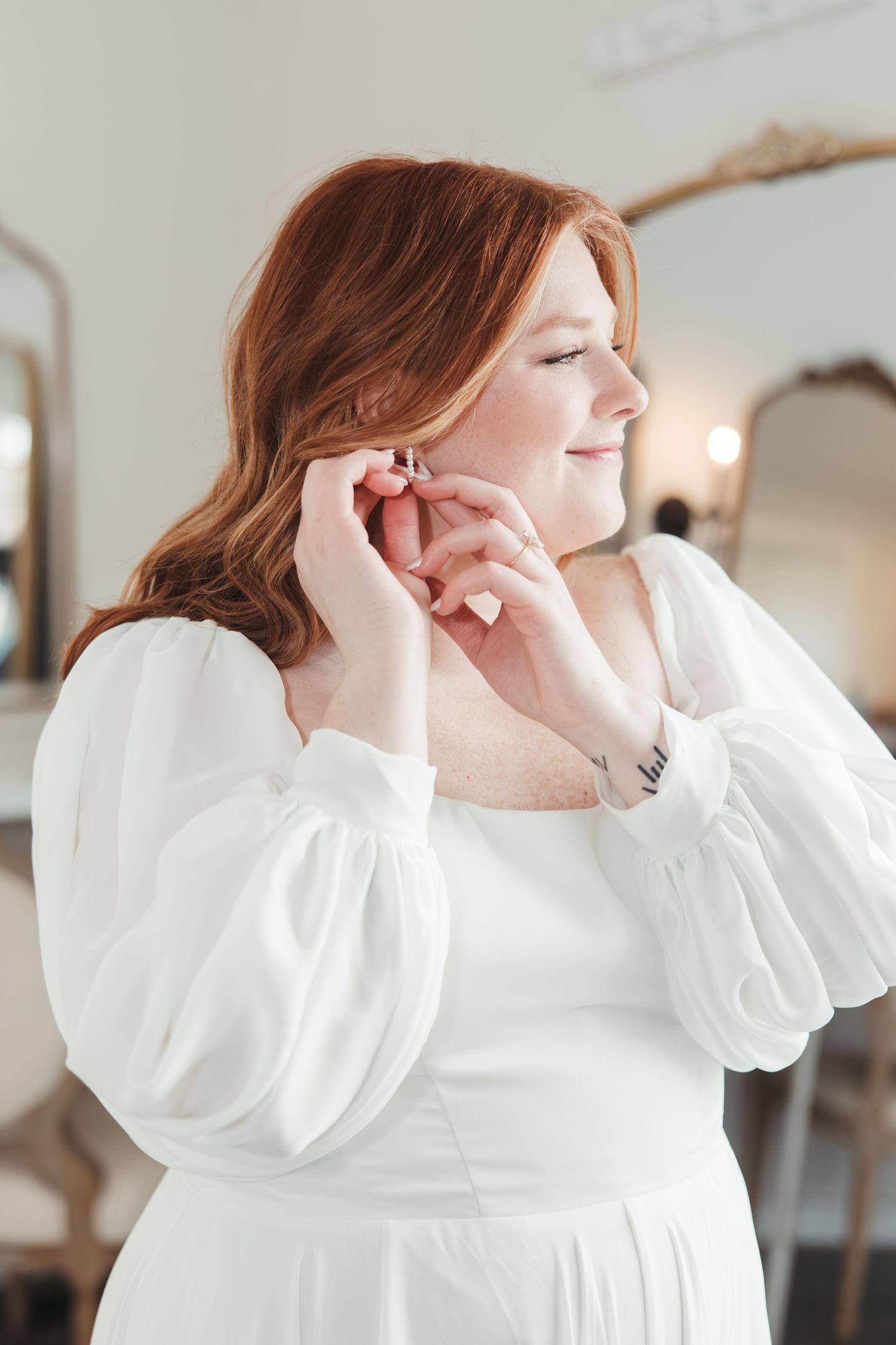 Classic bridal portrait in white dress with puffy sleeves putting on earrings.